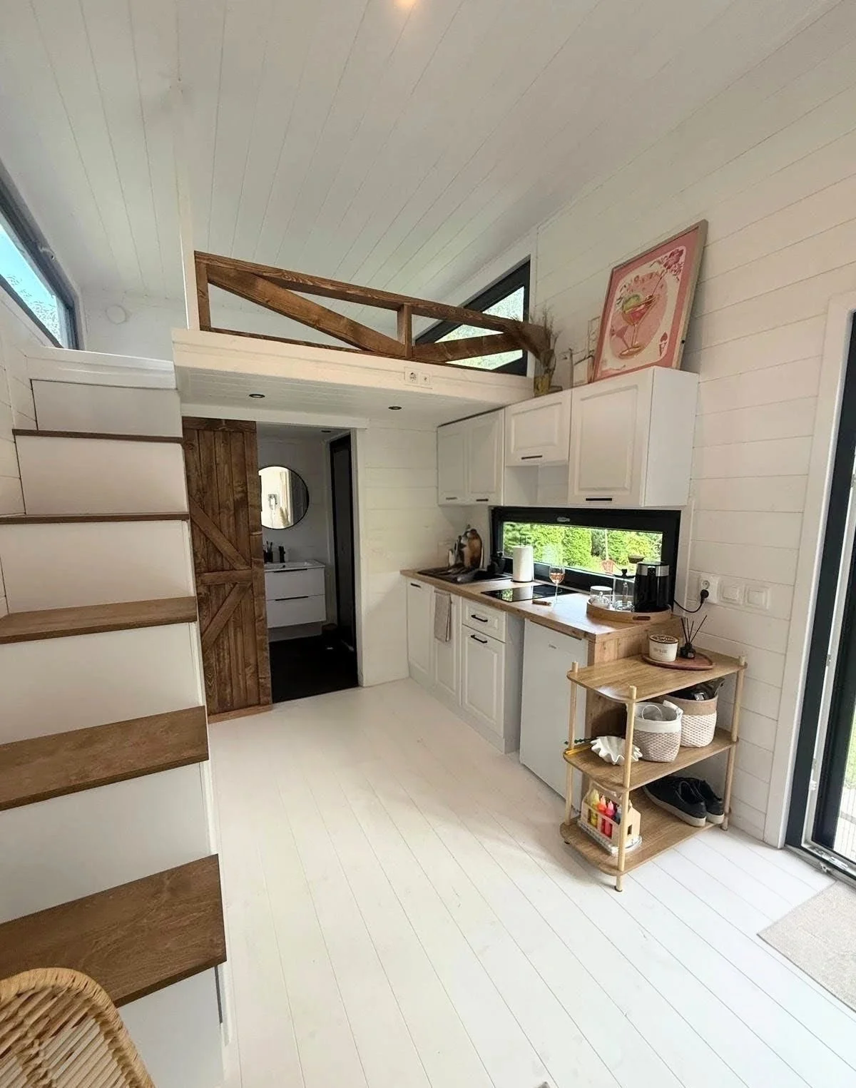 Eine moderne kleine Küche mit weißen Schränken, Holzarbeitsplatten und einer großen Fensteransicht, mit einem Steg im oberen Bereich, der als Schlafraum dient.