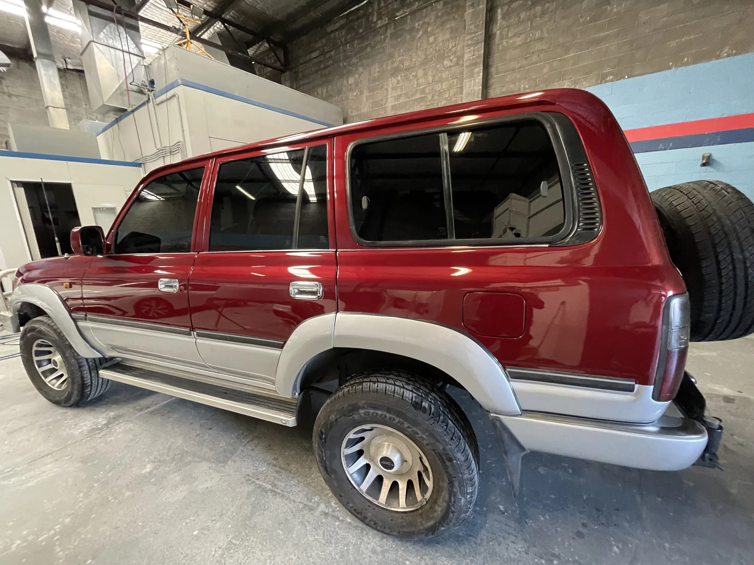 A red and silver SUV parked inside a warehouse with visible tires and industrial equipment in the background.