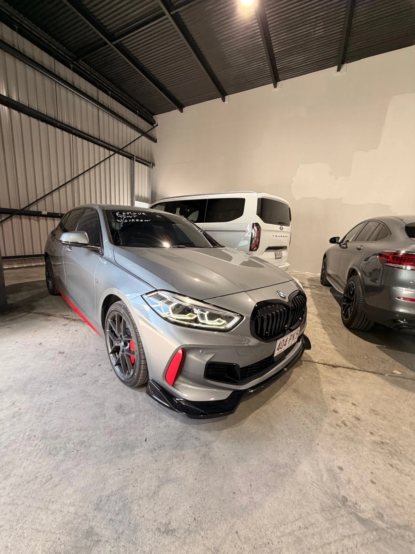 A silver BMW car with black and red accents parked inside a warehouse or garage alongside other vehicles.