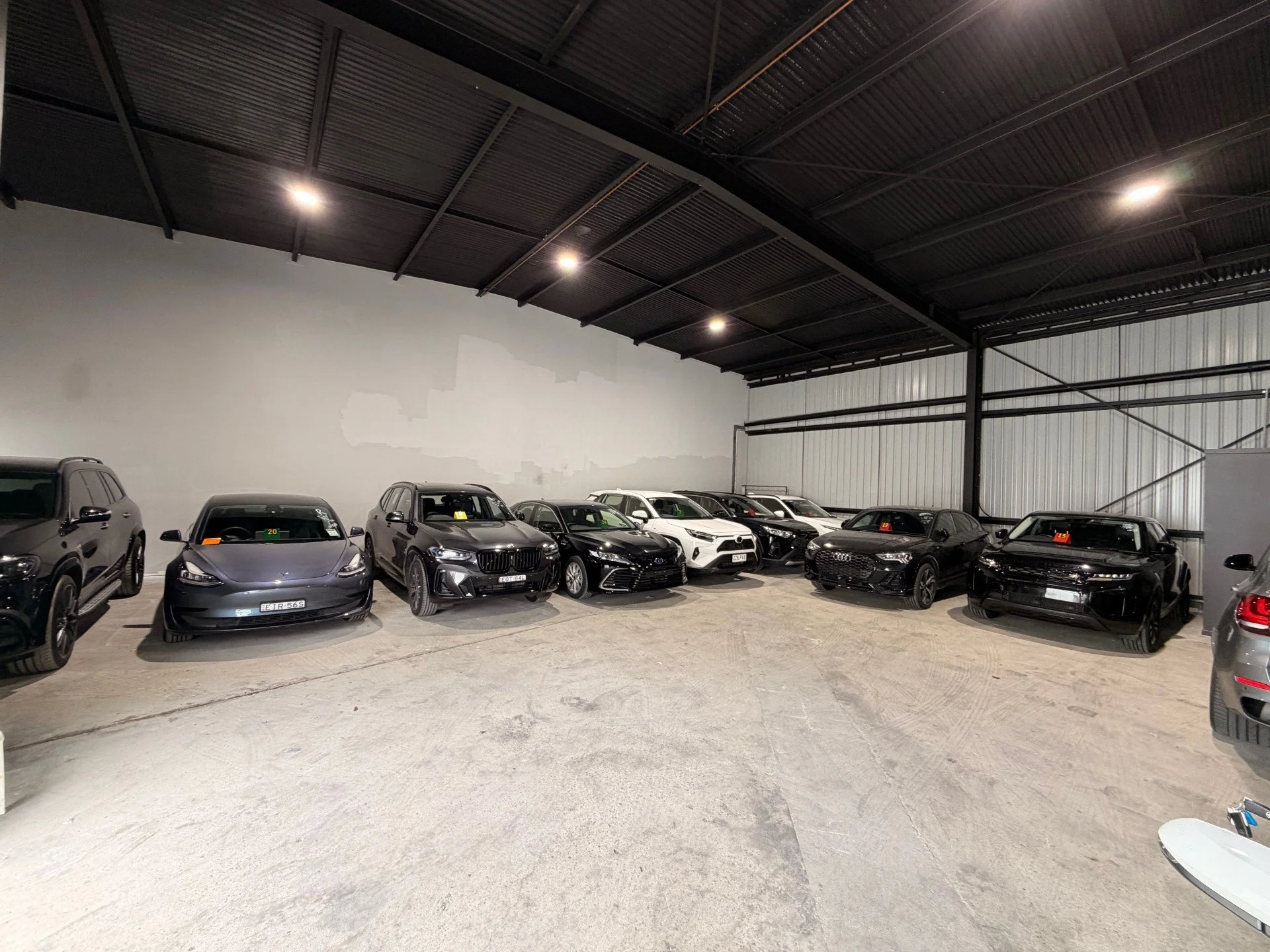 Indoor car storage with a variety of black, white, and gray cars parked in a large, well-lit warehouse with a high ceiling.
