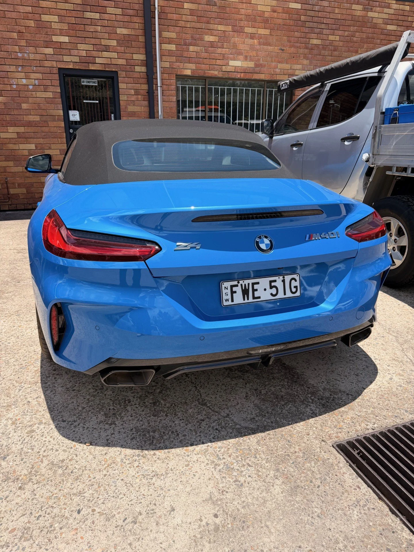 Blue BMW Z4 convertible with NSW license plate FWE-51G, parked on a concrete surface with a black convertible top and rear view visible.