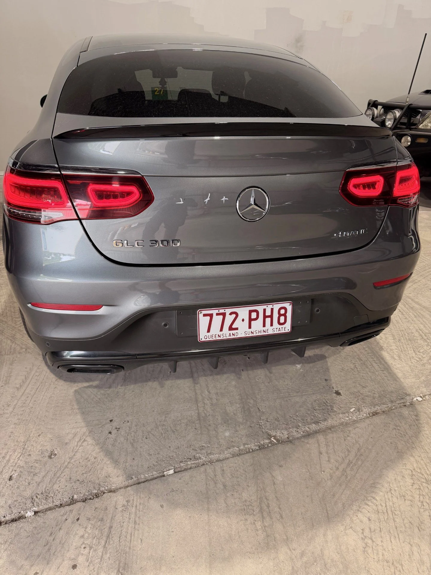 Rear view of a gray Mercedes-Benz GLC 300 4MATIC SUV with Queensland license plate 772-PH8, parked on a concrete surface in an indoor parking garage.