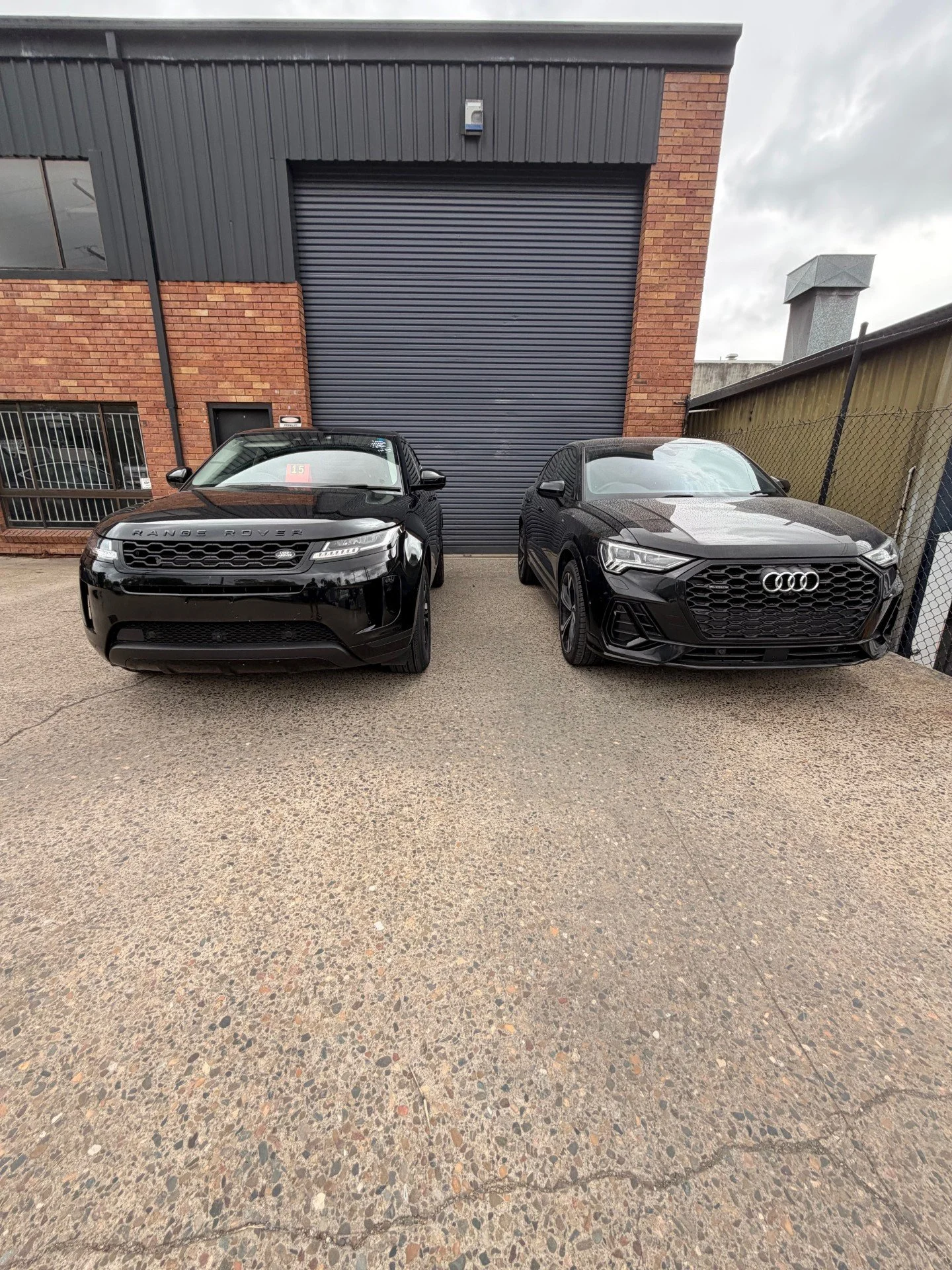 A black Range Rover and a black Audi parked side by side in front of a large gray garage door.