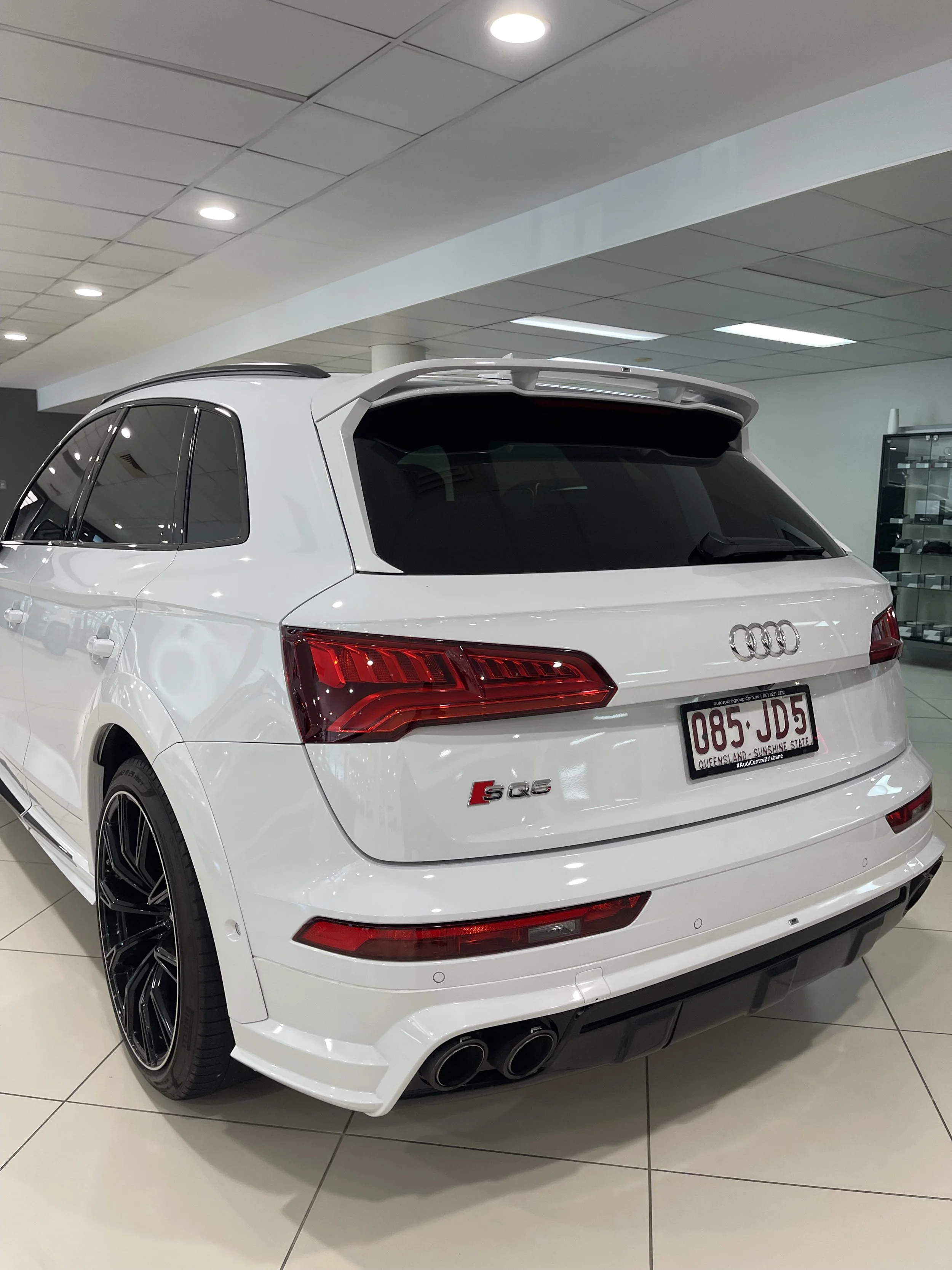 White Audi S Q5 SUV with dual exhaust pipes displayed in a showroom.