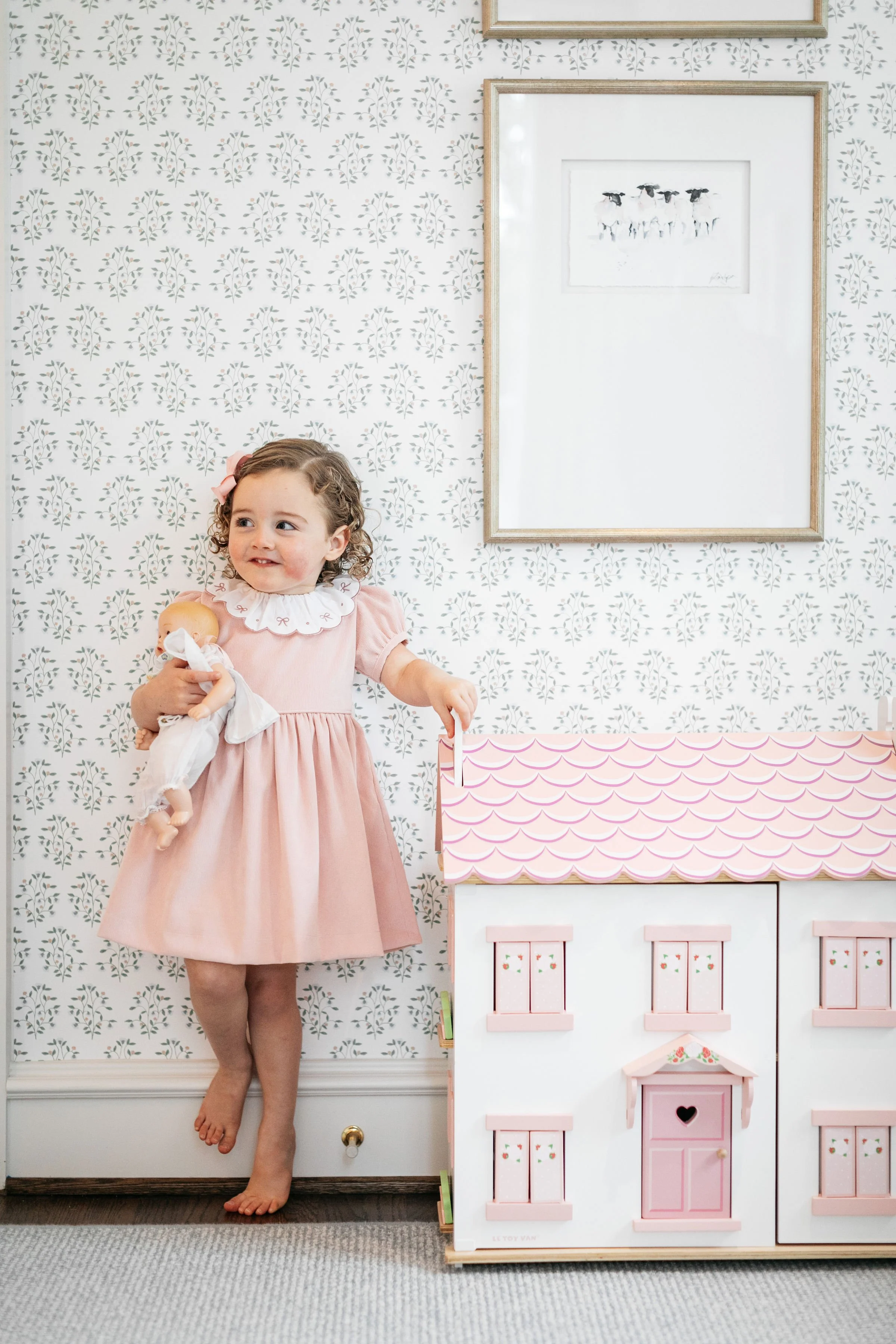 little girl wearing a pink dress standing next to a pink dollhouse