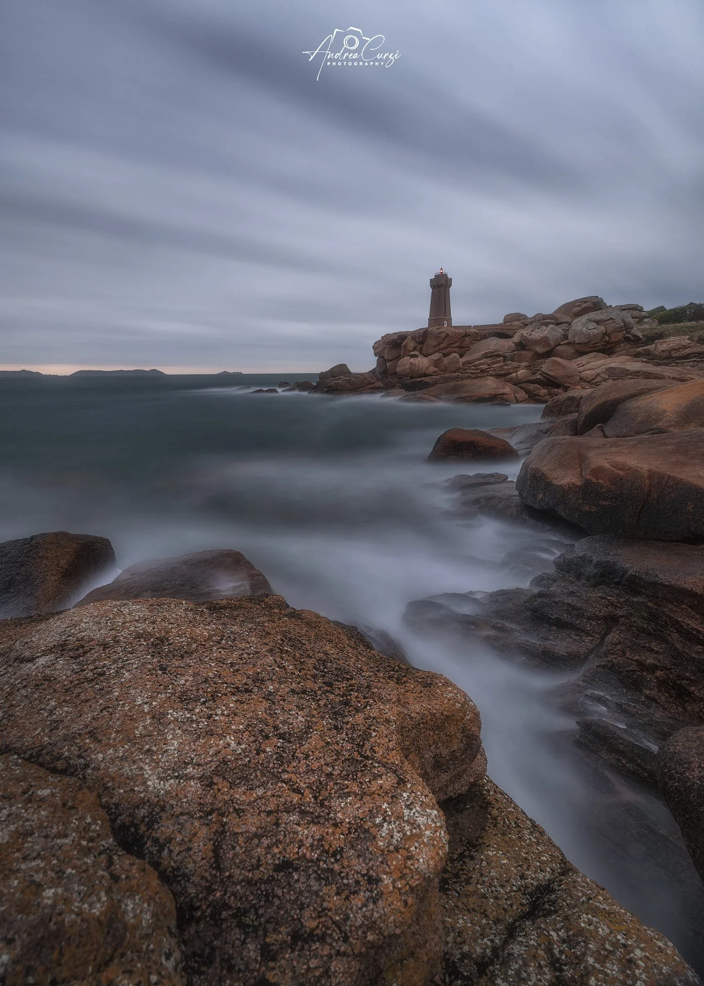 Faro di Ploumanac'h in Bretagna con la costa di granito rosa, il faro in lontananza, cielo nuvoloso e acque mosse