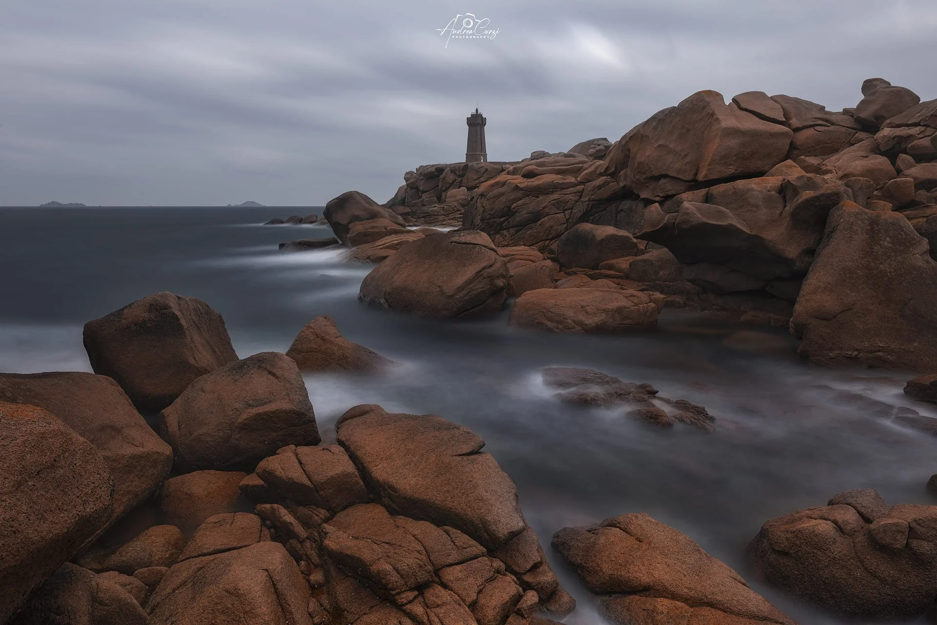 Faro di Ploumanac'h in Bretagna con un faro sulla cima, mare in movimento, cielo nuvoloso, paesaggio costiero e la costa di granito rosa.