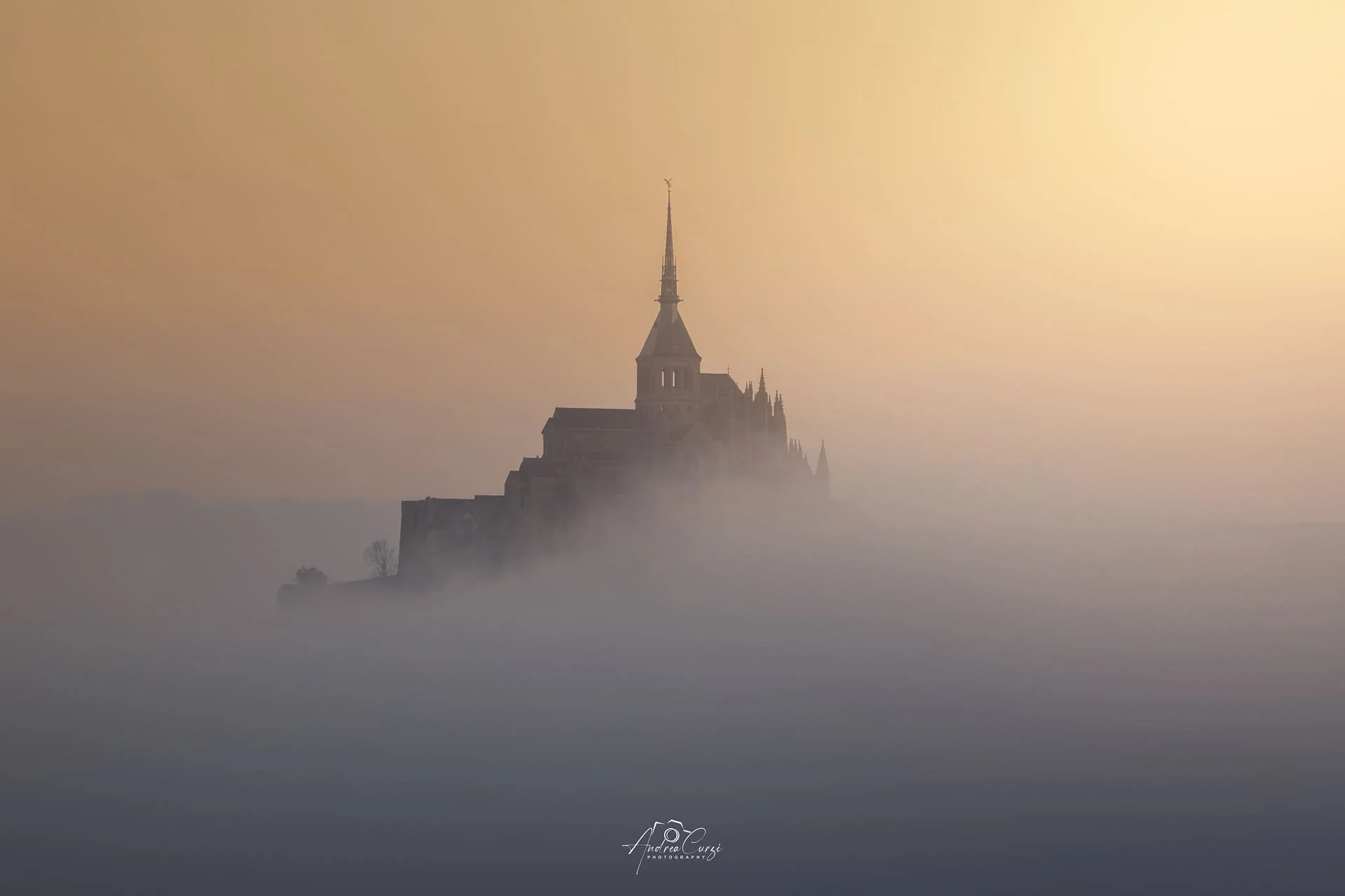 Monte sacro avvolto dalla nebbia con una chiesa in siluetta, al tramonto.