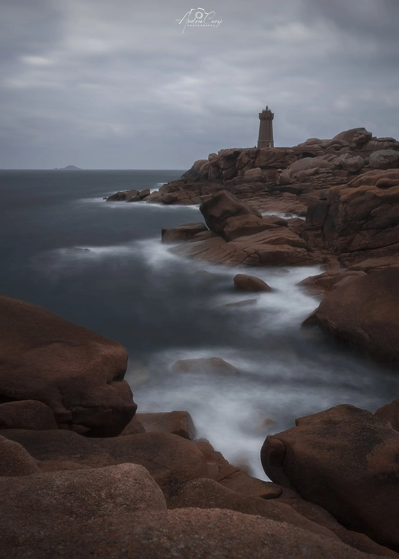Faro di Ploumanac'h in Bretagna con la costa di granito rosa, il faro in lontananza, cielo nuvoloso e acque mosse