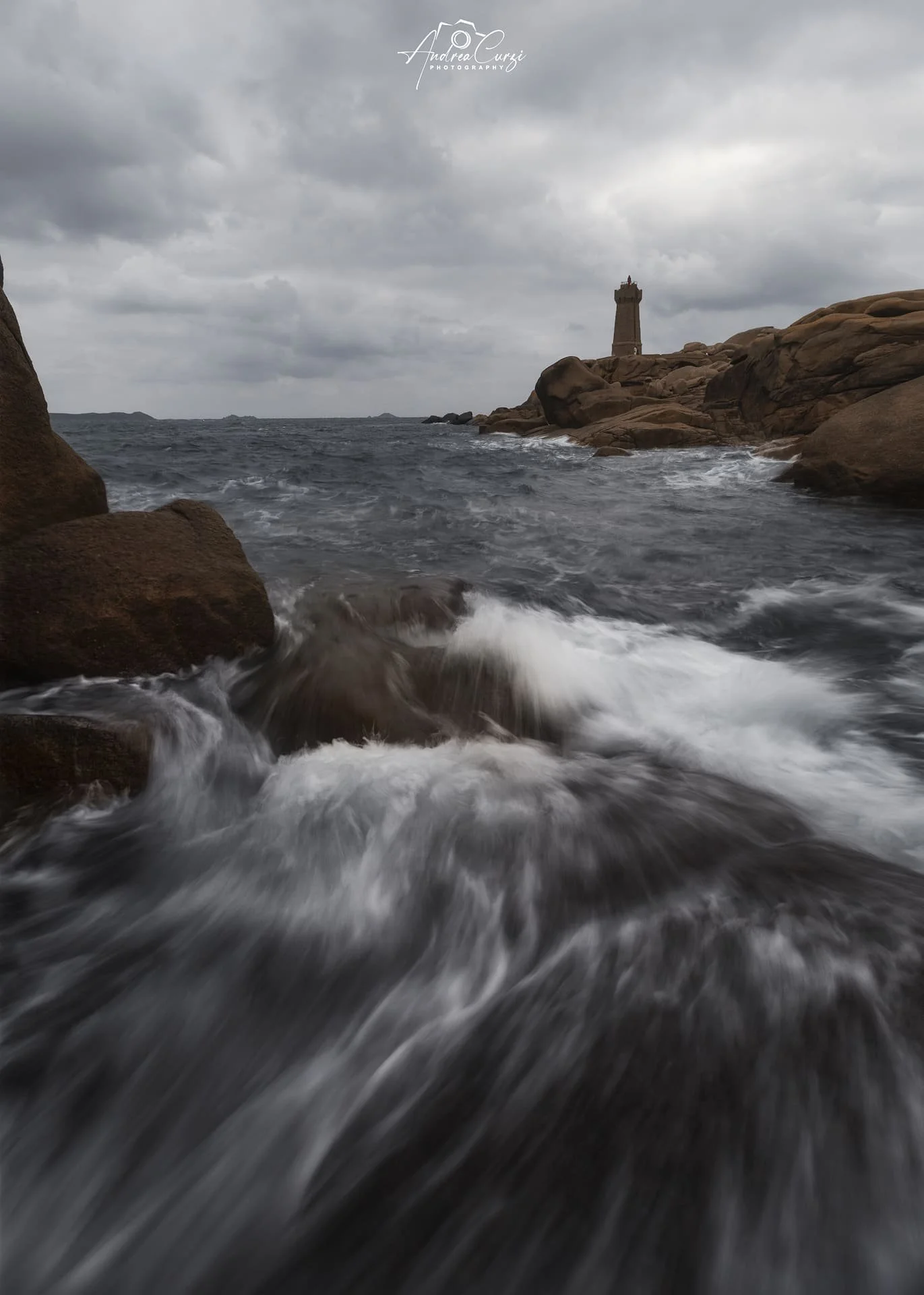 Faro di Ploumanac'h in Bretagna sulla costa di granito rosa con onde che si infrangono, faro in lontananza e cielo nuvoloso