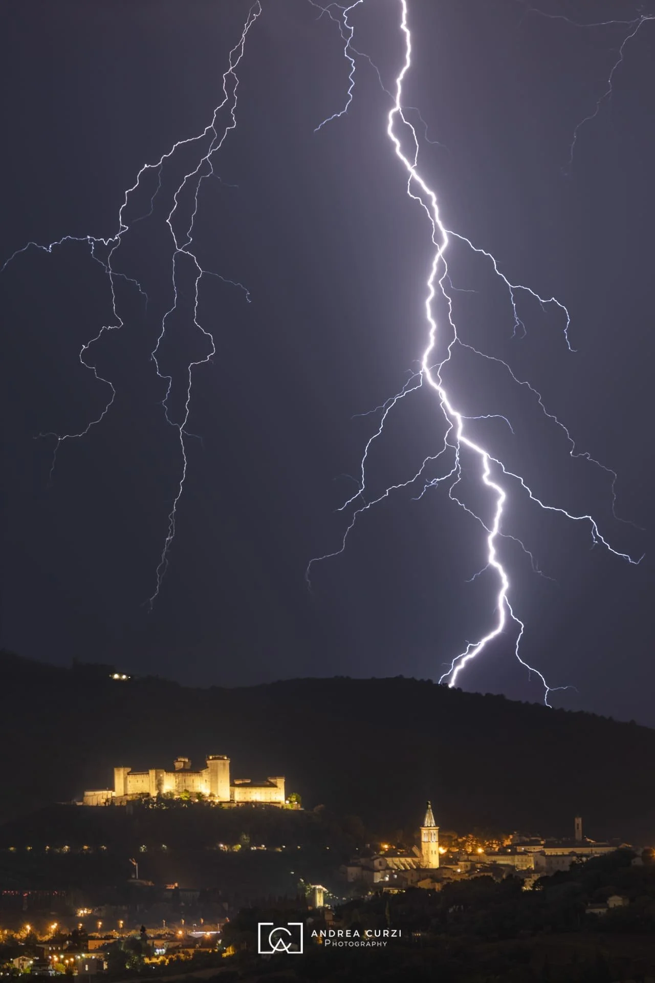 Fulmine durante un temporale sopra un castello e una chiesa in una città. Scatta a Spoleto durante un workshop fotografico di Andrea Curzi
