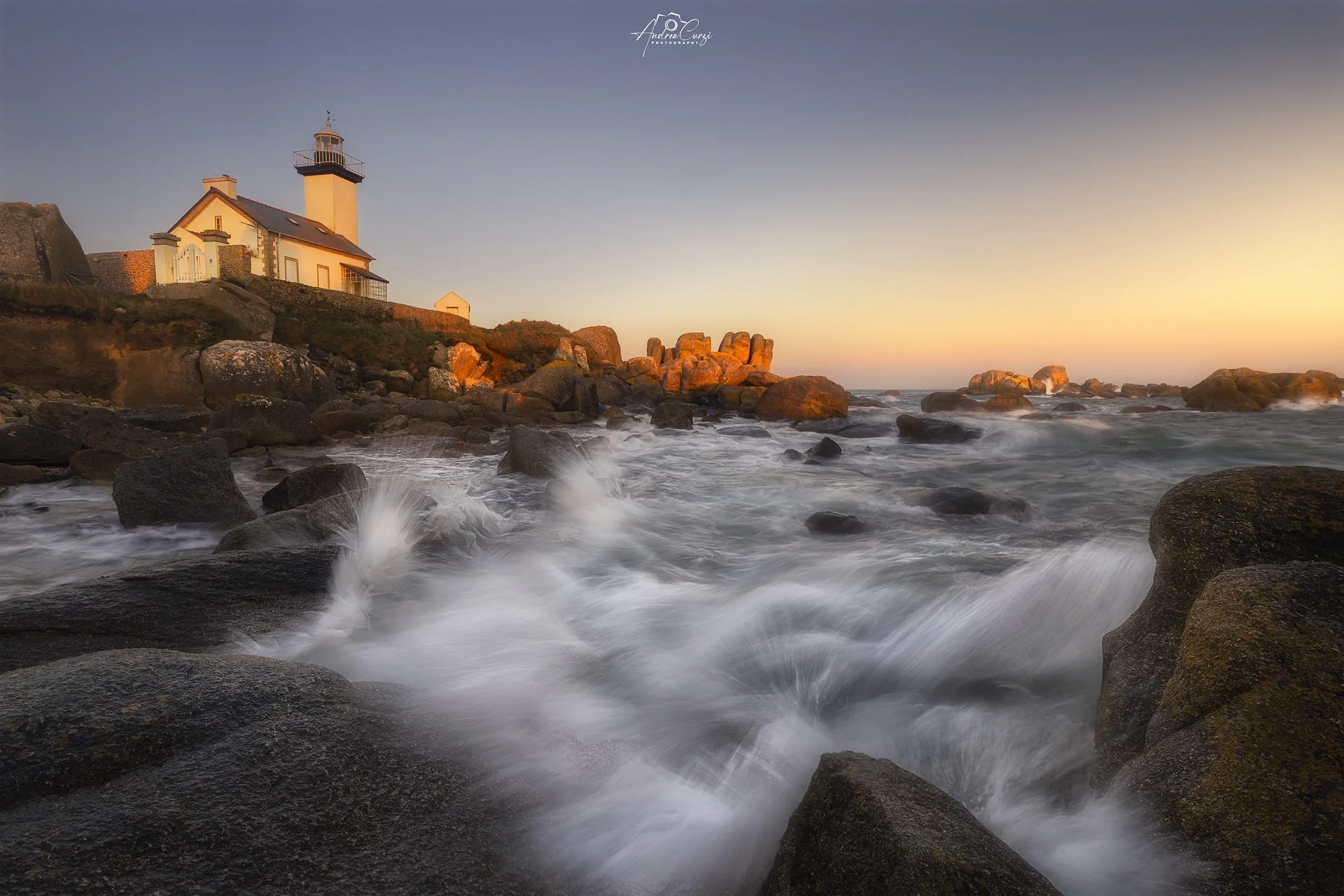 Faro di Pontusval in Bretagna sulla costa rocciosa al tramonto con onde che si infrangono sui sassi