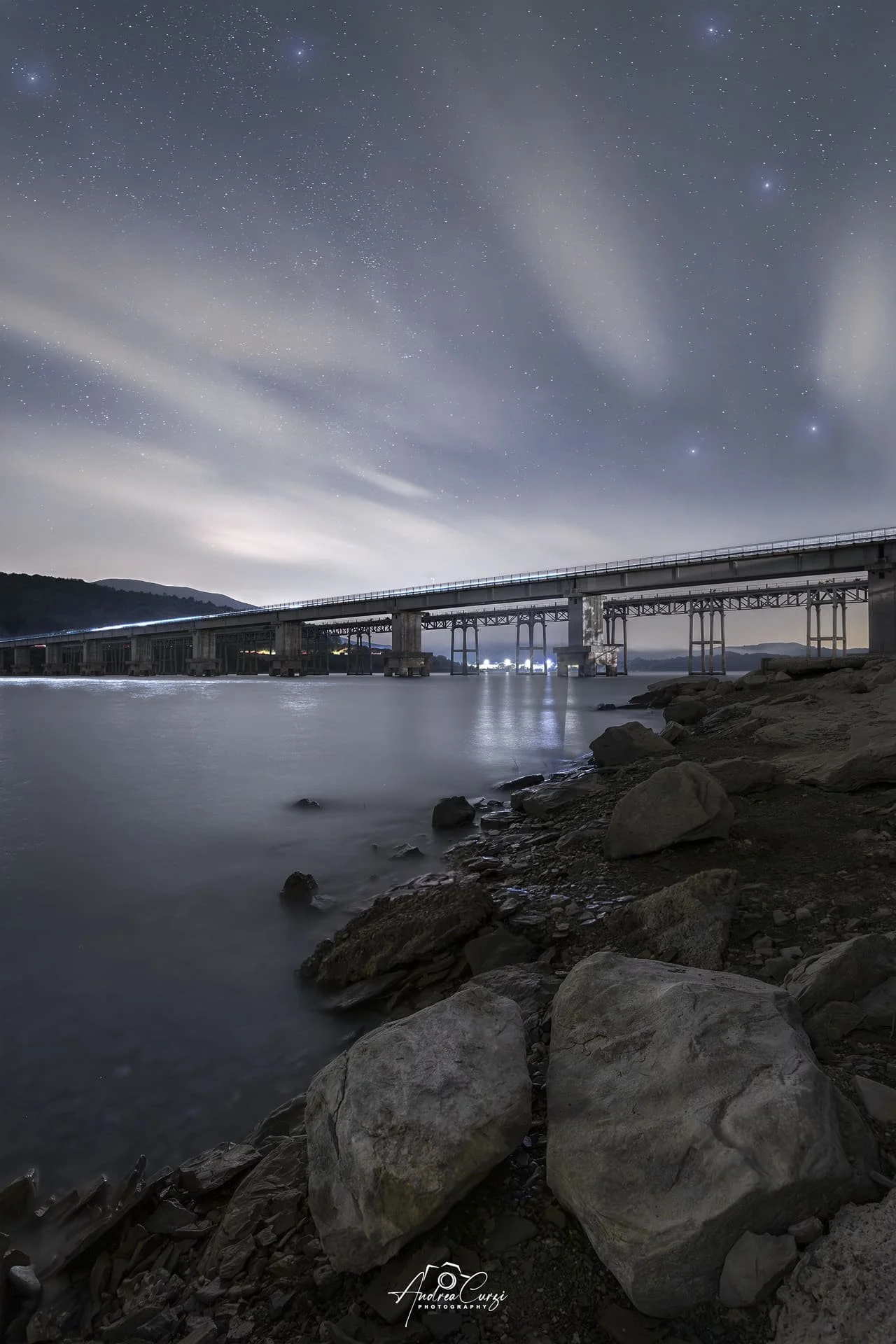 Veduta notturna di un ponte sopra un fiume con cielo stellato e nuvole