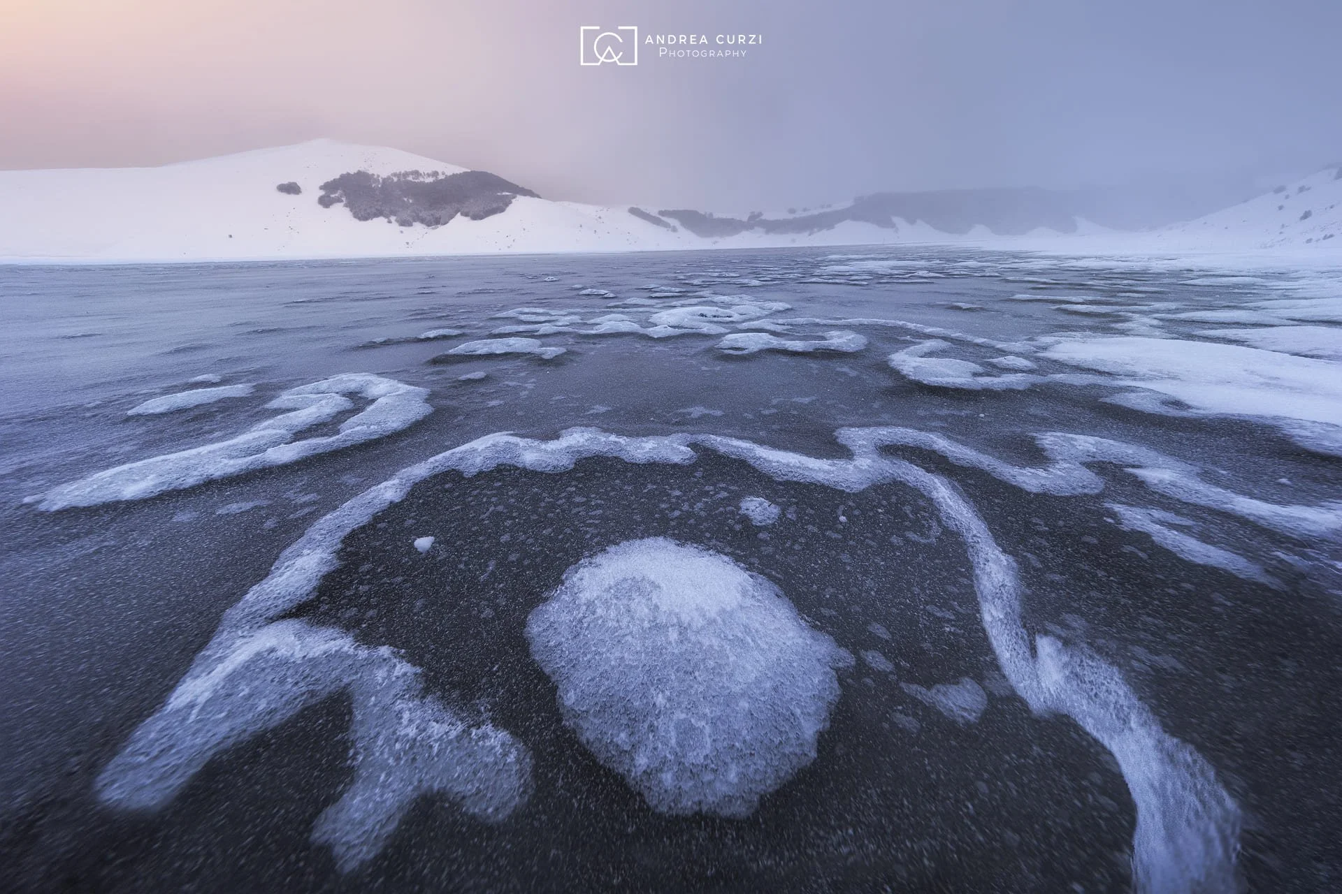 Paesaggio glaciale con calotte di ghiaccio e montagne innevate in lontananza. Scattata sul Parco Nazionale dei Monti Sibillini a Castelluccio di Norcia durante un workshop fotografico di Andrea Curzi.