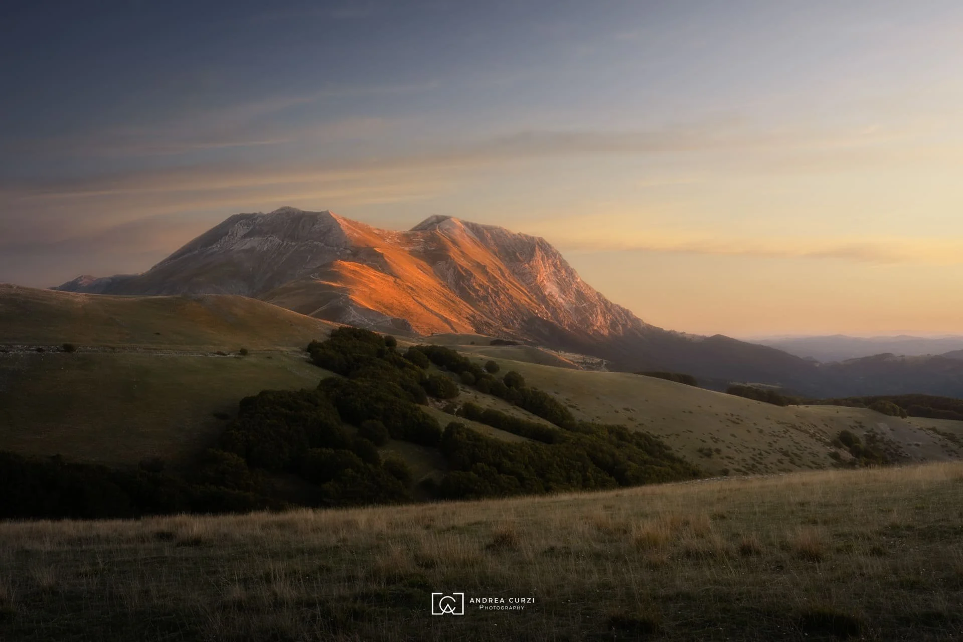 Paesaggio montano al tramonto con montagne e colline verdi. Scattata sul Parco Nazionale dei Monti Sibillini nelle Marche durante un workshop fotografico di Andrea Curzi.