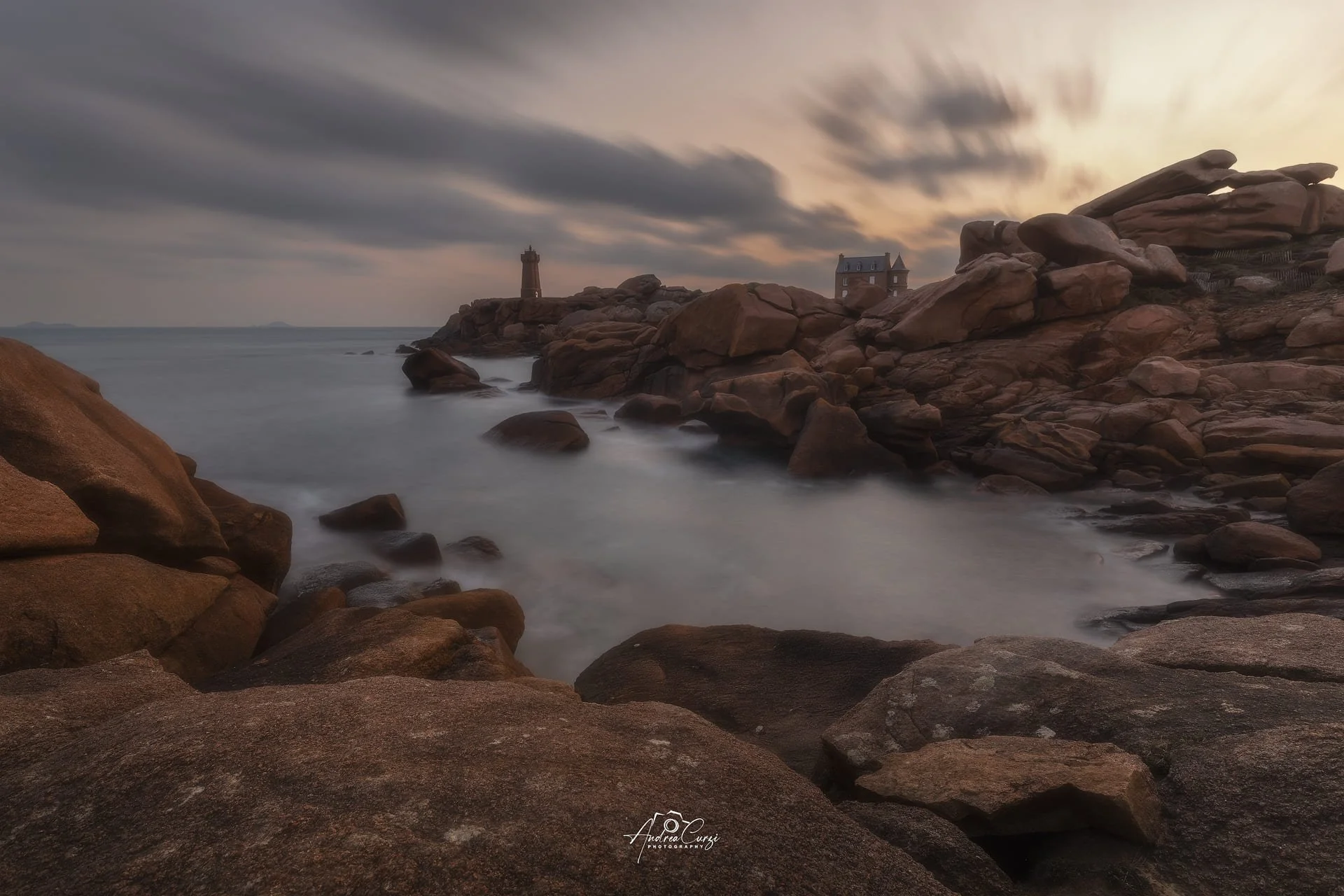 Faro di Ploumanac'h in Bretagna con costa di granito rosa all'alba con due antichi fari e una piccola casa sulla scogliera, cielo nuvoloso