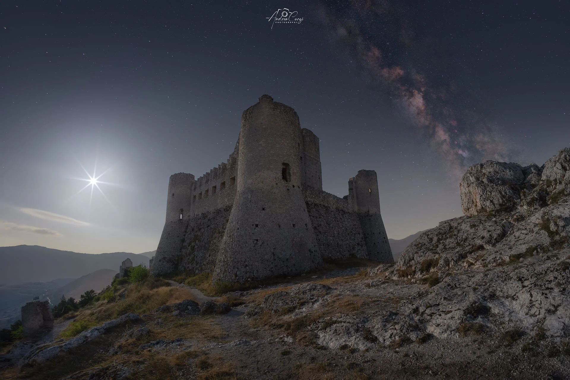 Castello di Rocca Calascio in abruzzosotto un cielo notturno con la Via Lattea e una luna brillante in alto a sinistra