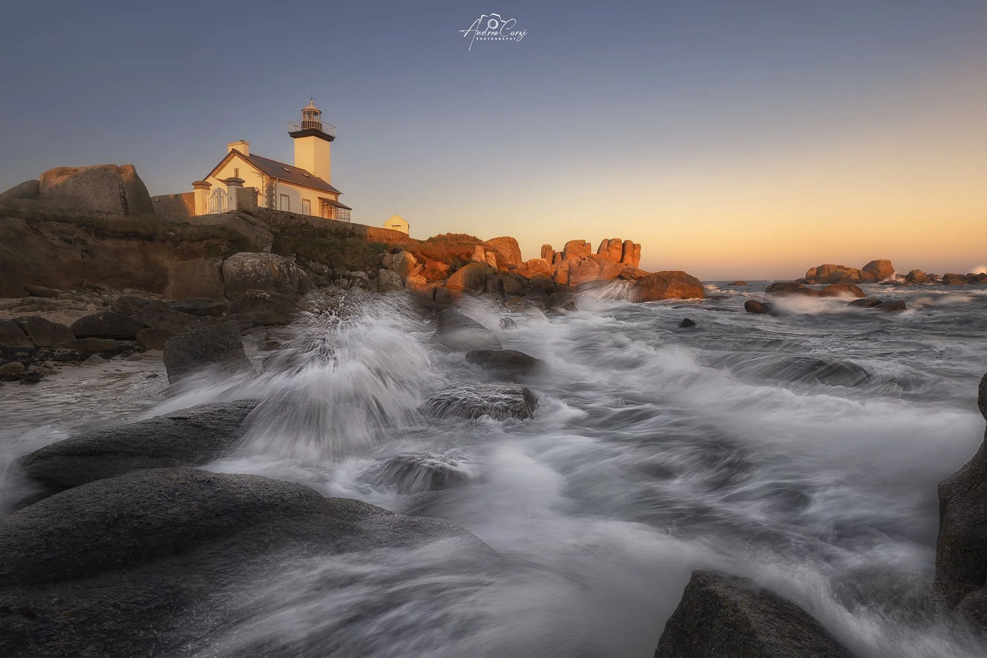 Faro di Pontusval in Bretagna sulla costa rocciosa al tramonto con onde che si infrangono sui sassi