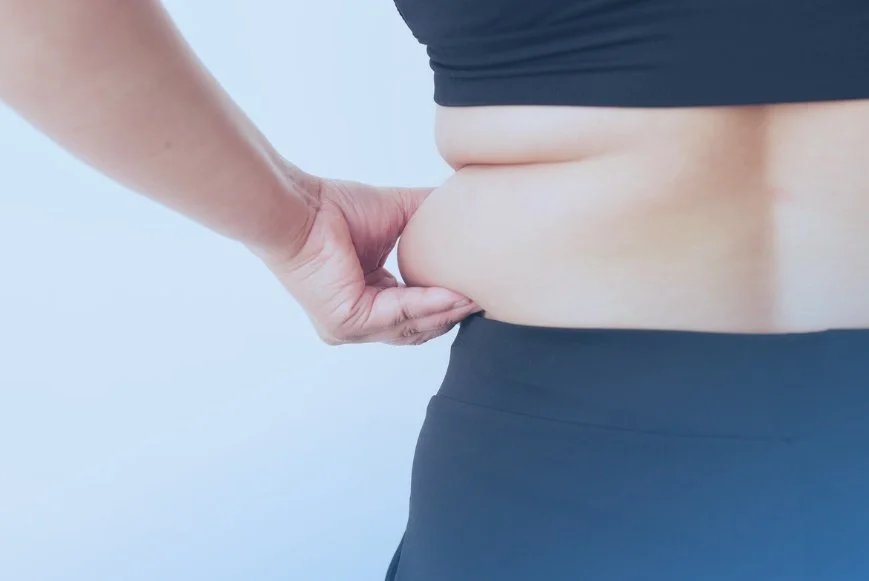 woman grabbing skin roll on side, showing dangers of visceral fat even in skinny people. Get a Dexa Scan at DexaFit West Houston, TX
