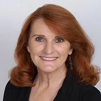 Portrait of a woman with red hair, smiling, wearing earrings and a black top.