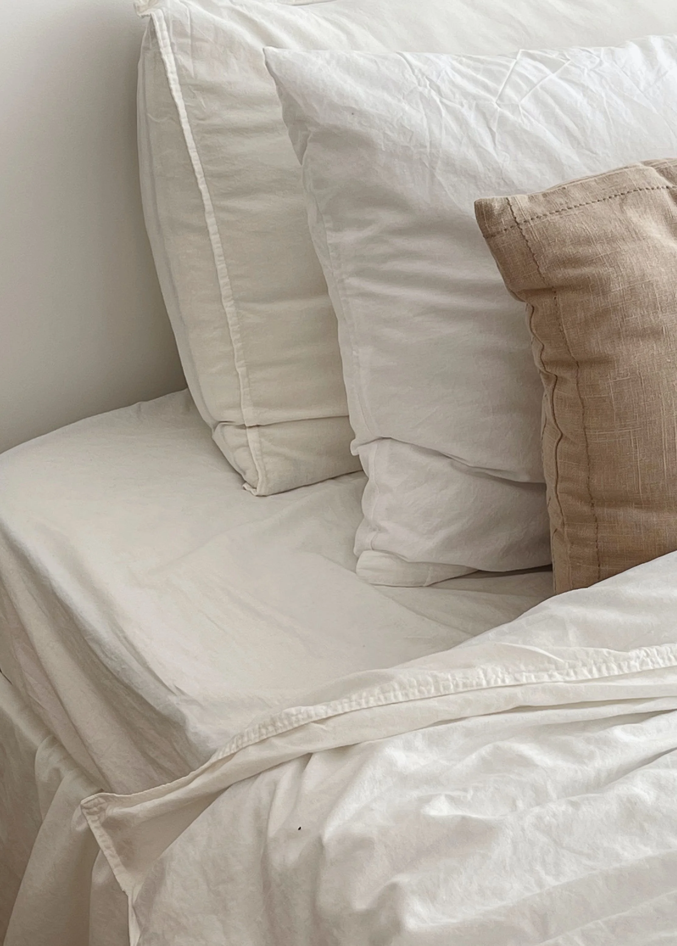 A neatly made bed with white sheets and pillows, including one brown decorative pillow.