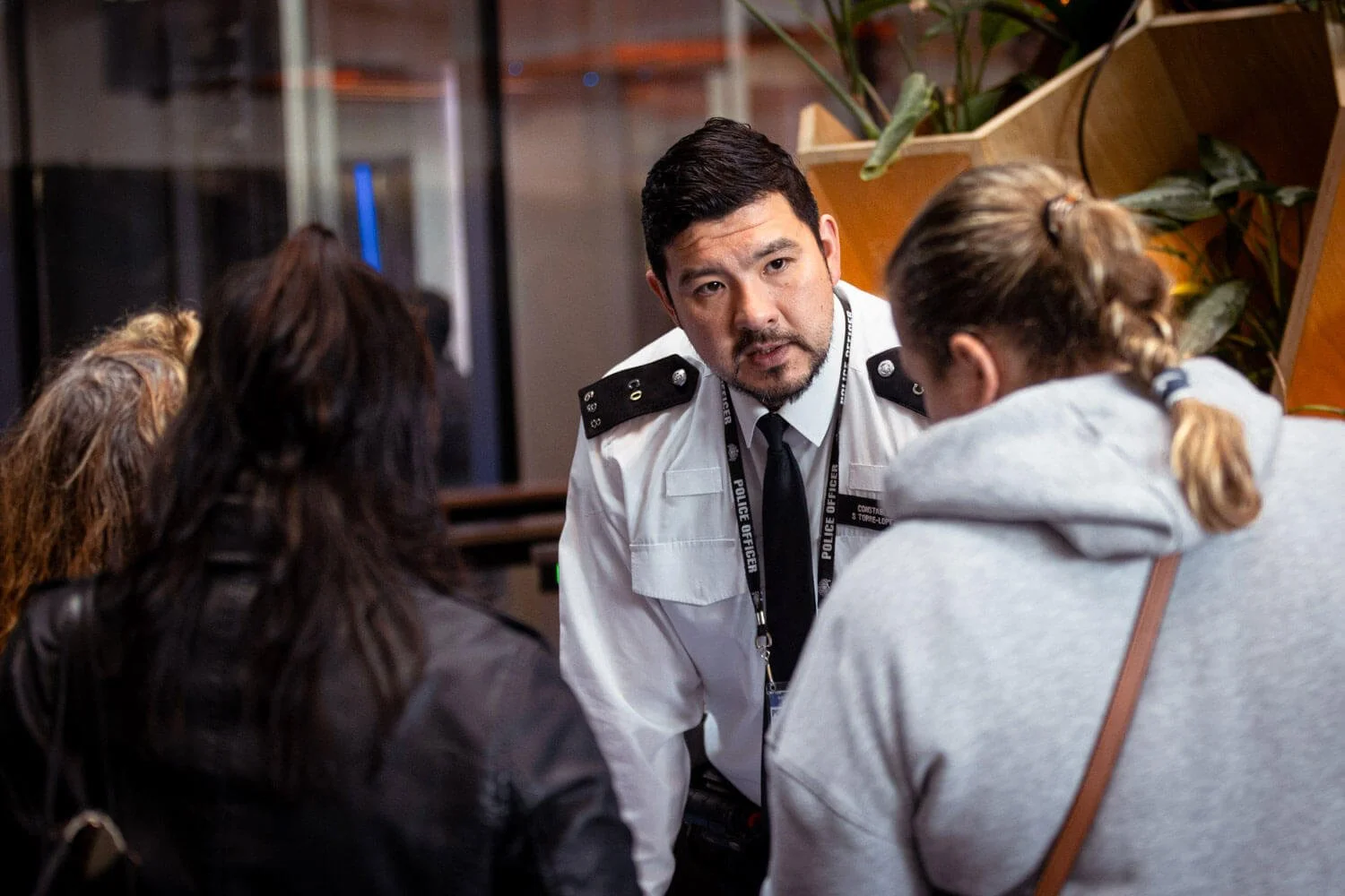 A police officer in uniform consulting with three women in a public indoor space.