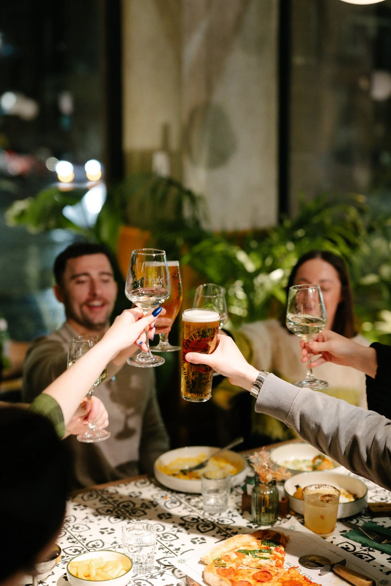 Friends raising wine glasses and pints around a table at Amelia Hall, Belfast.