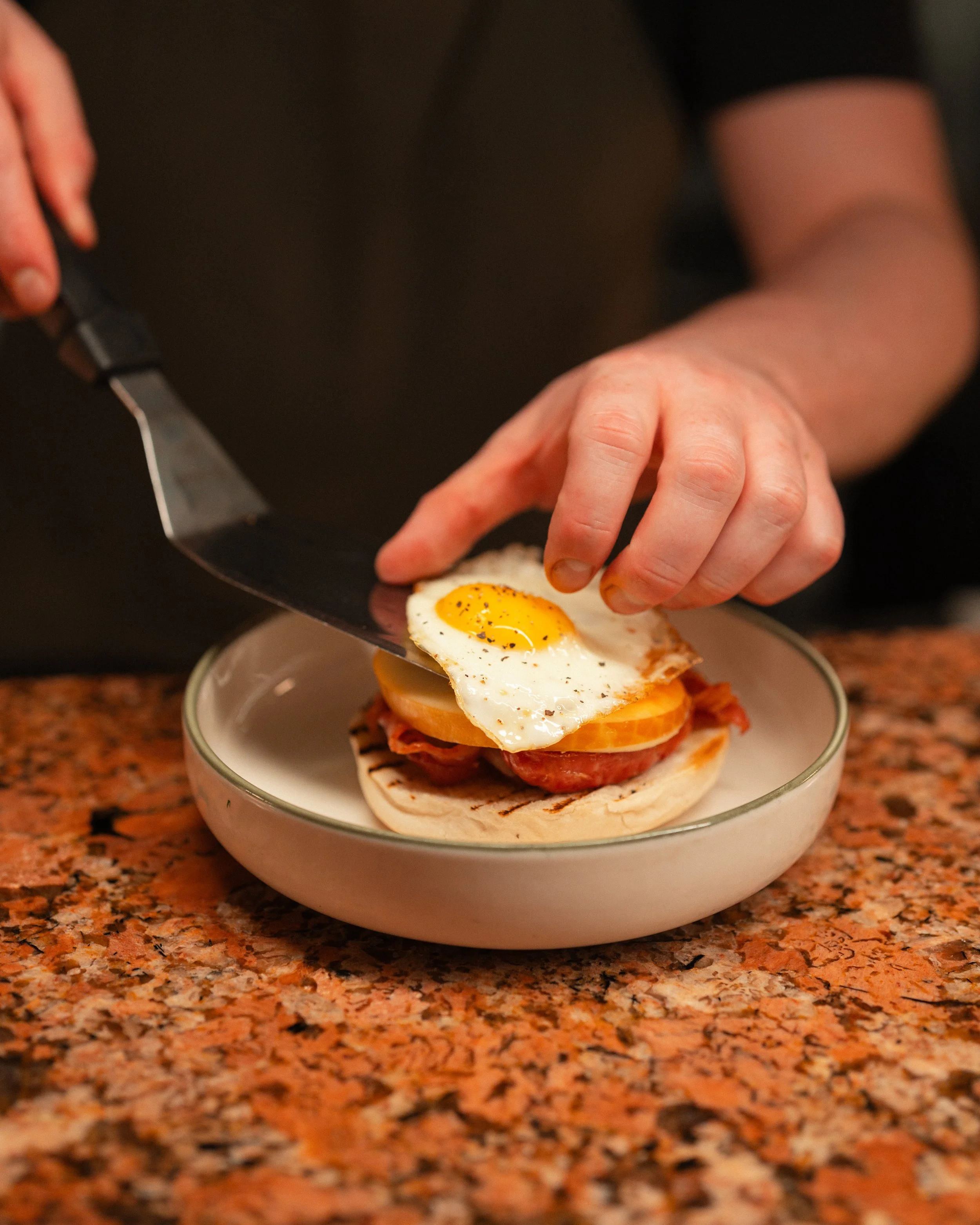 Chef topping a breakfast muffin with a fried egg in the kitchen at Amelia Hall, Belfast.