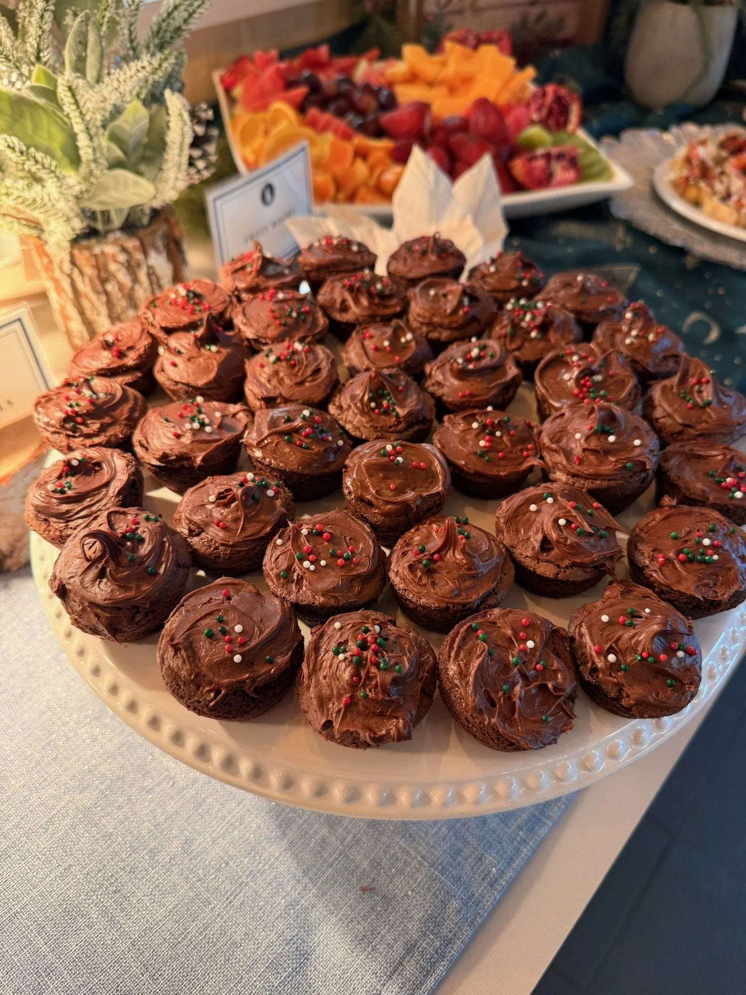 Chocolate cupcakes decorated with red, green, and white sprinkles on a white platter.