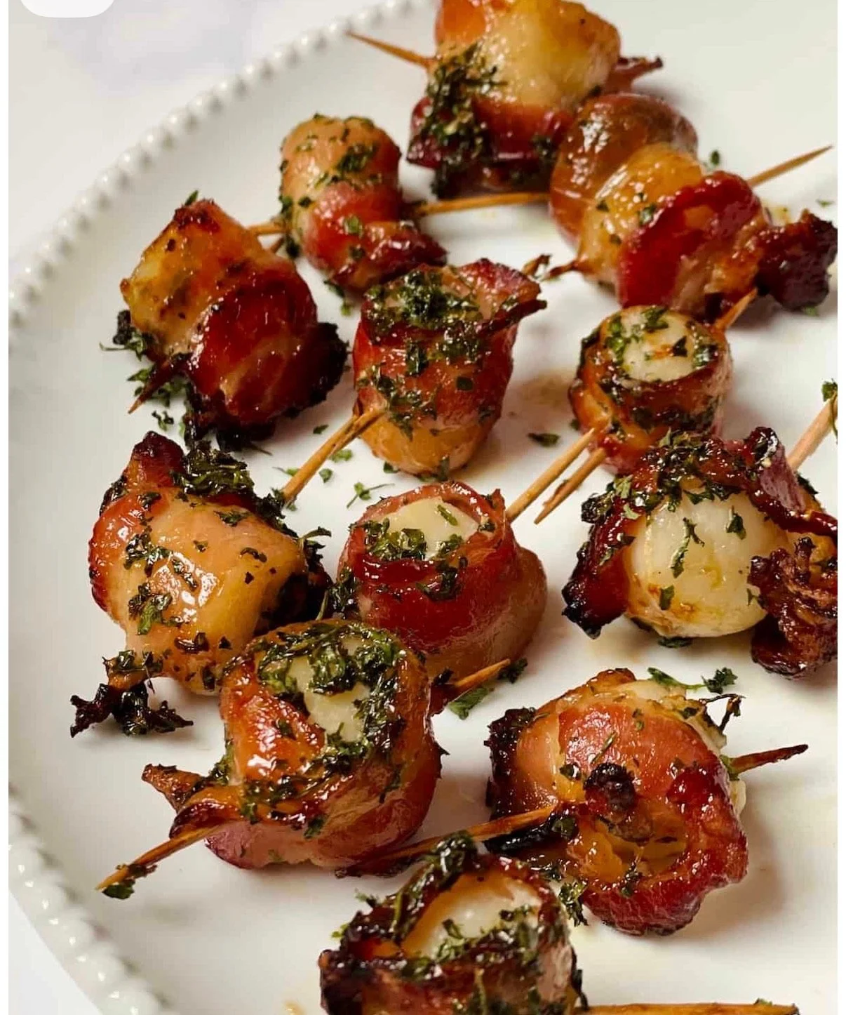 Close-up of bacon-wrapped stuffed medallions garnished with herbs on a white plate.