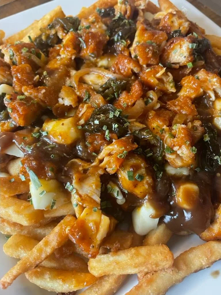 Plate of loaded French fries topped with gravy, cheese, chicken pieces, and chopped green onions.