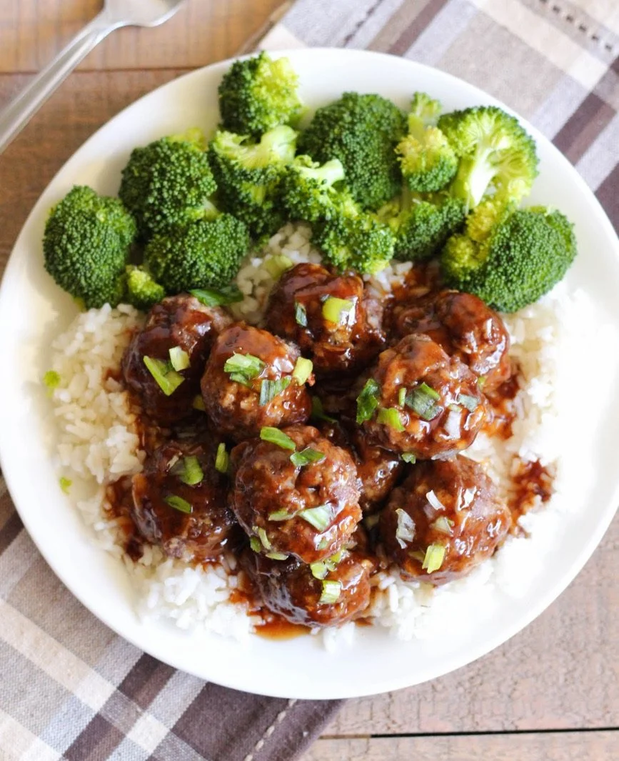 A white bowl filled with rice topped with glazed meatballs and steamed broccoli.