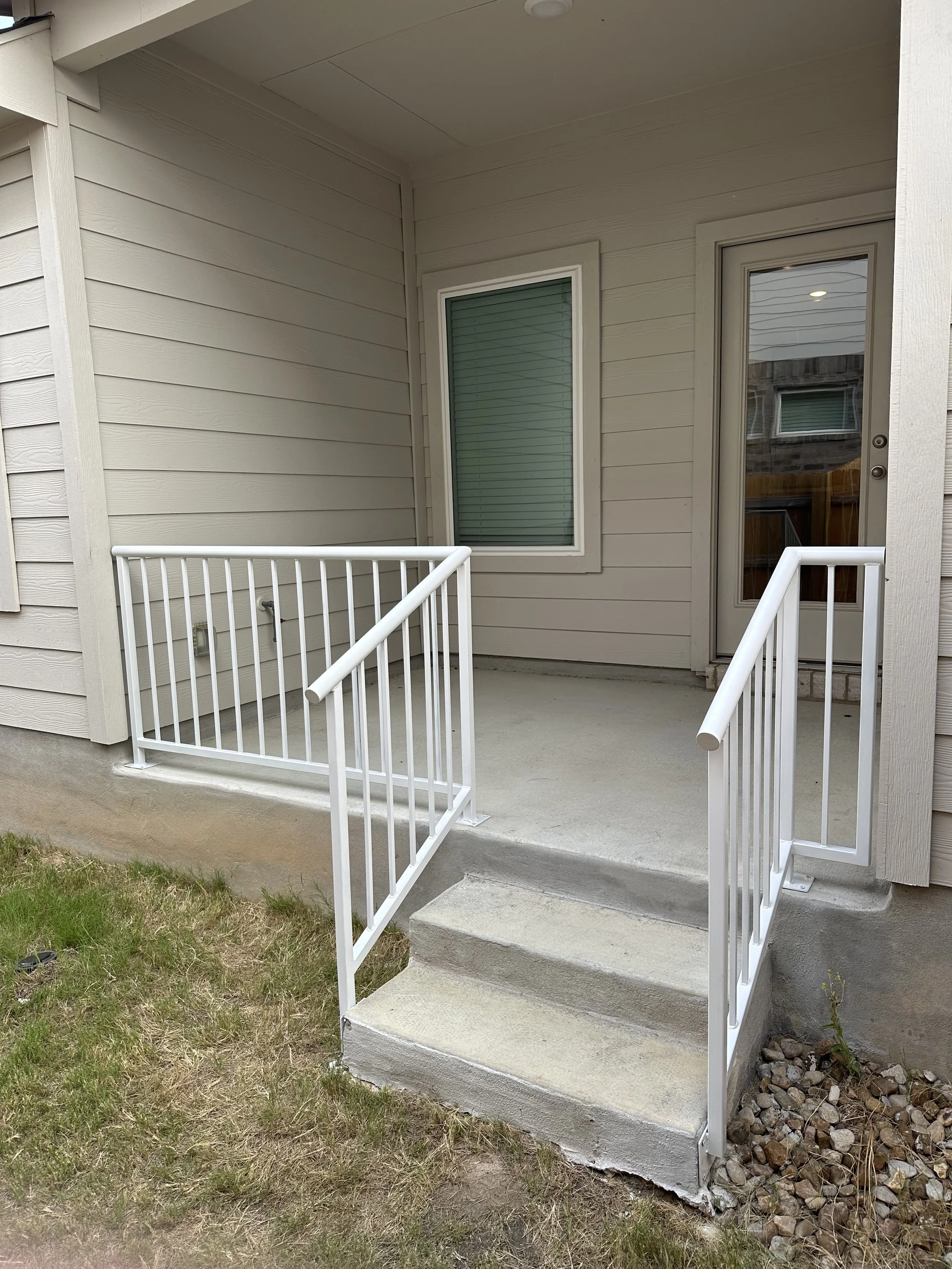 A small porch with concrete steps, a metal railing, and a white door with a glass window.