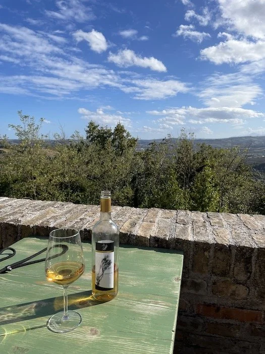 Bottle and glass of white wine on a wooden table with scenic countryside view in Fano, Italy.