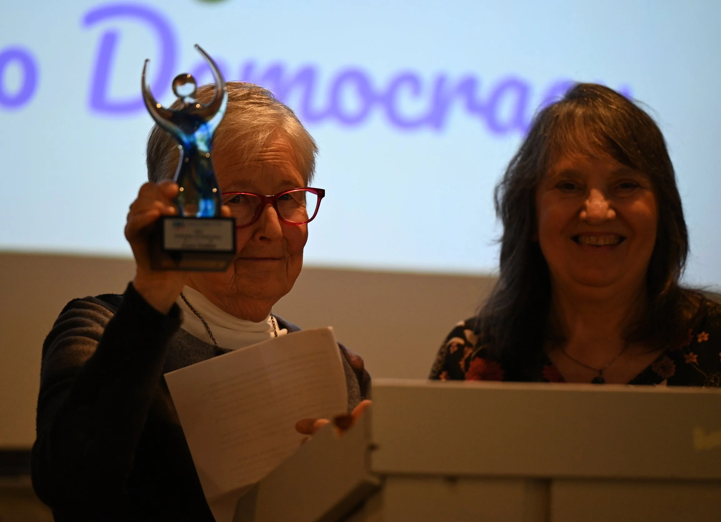 Defender of Democracy Laura Gotlieb holding art glass award at the podium with President Sue Jennik.