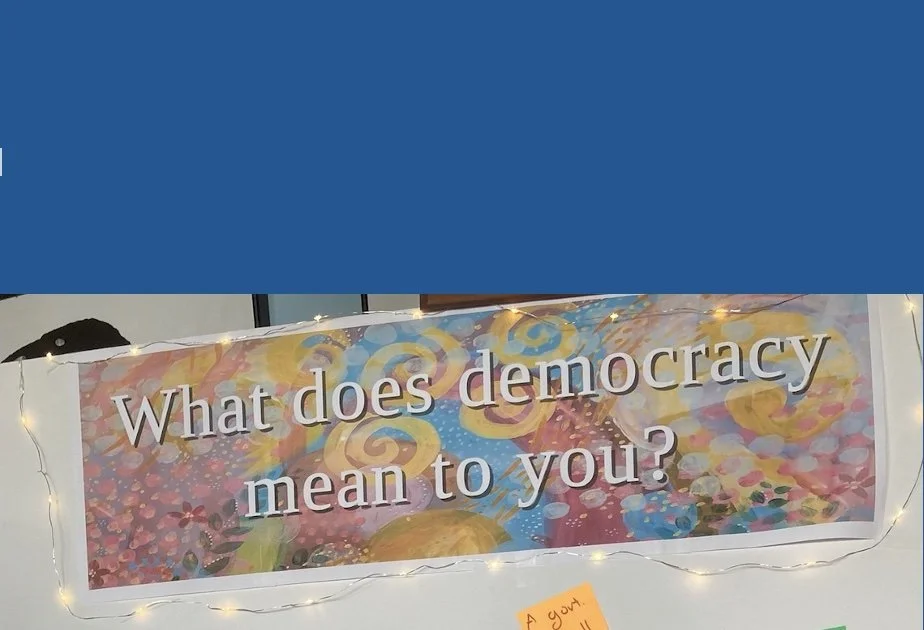 colorful sign: What does democracy mean to you?  with a string of white lights around it 