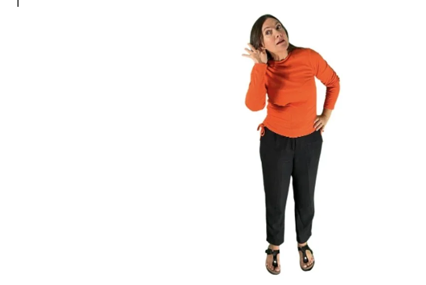 Woman with her hand to her ear, slightly bending and looking to her right as though trying to hear something.