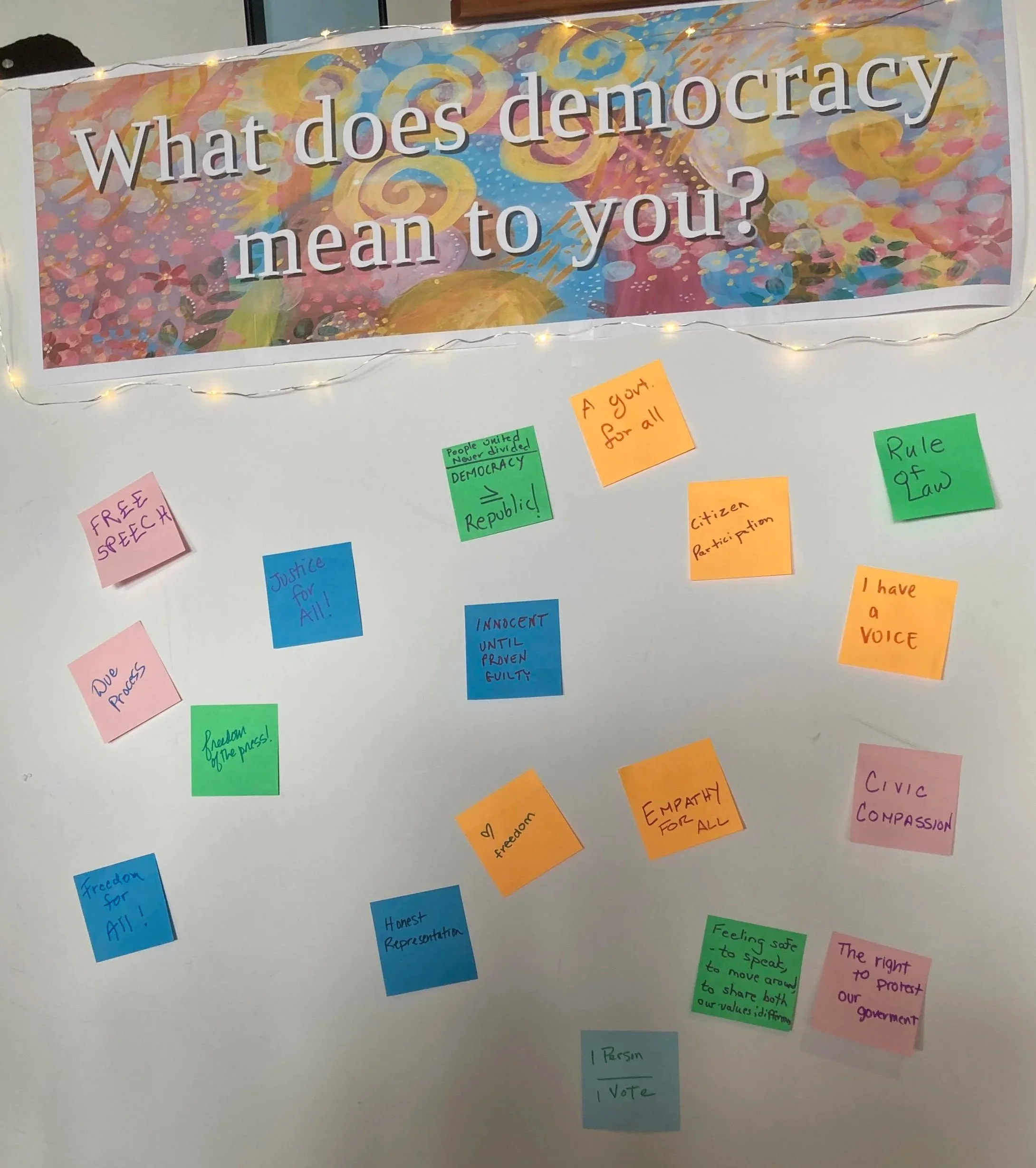 White board with question: What does democracy mean to you? and many sticky notes with answers.