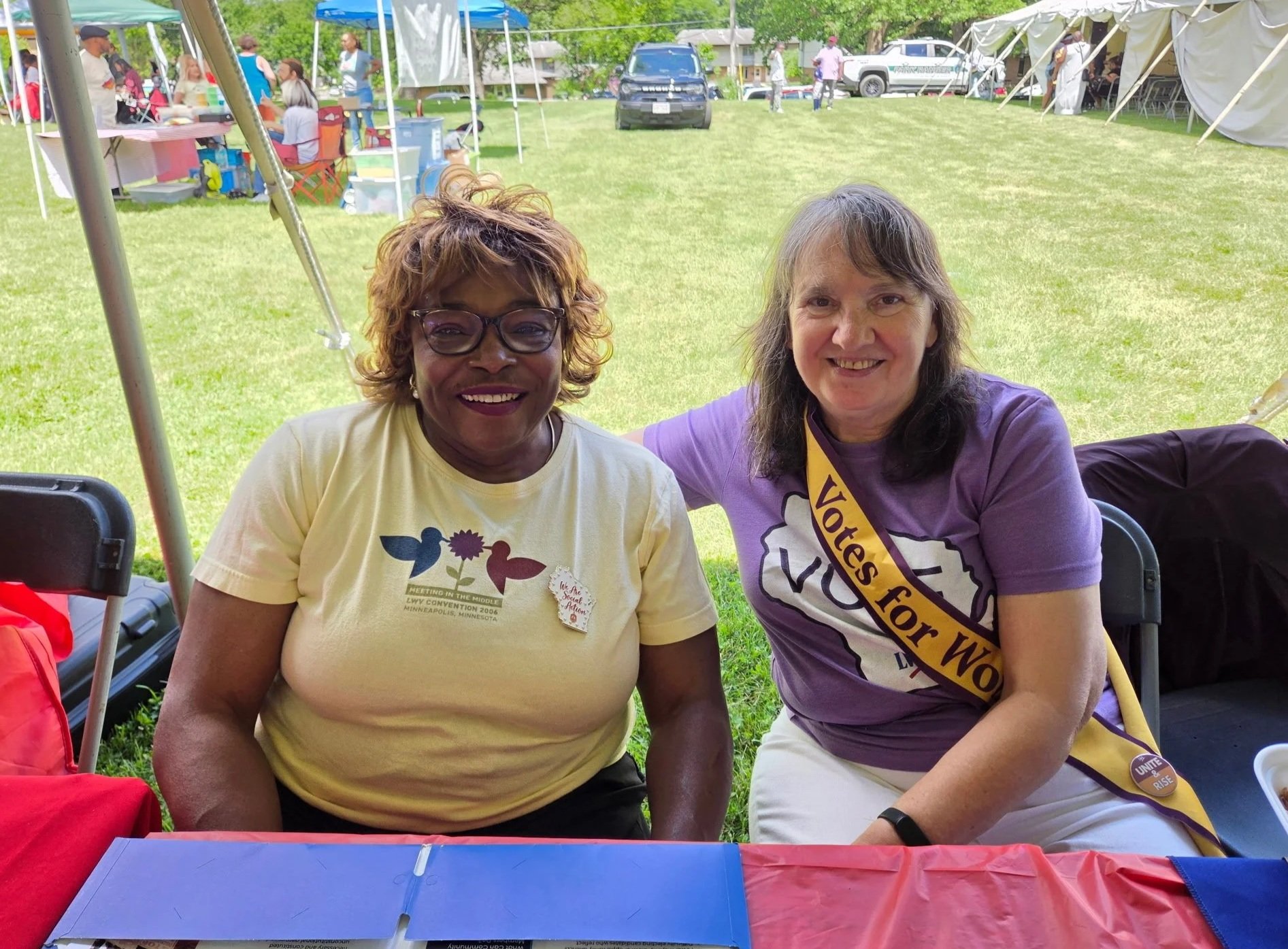 Earnestine Moss and Sue Jennik (wearing a Votes for Women sash) at a table at Penn Park.