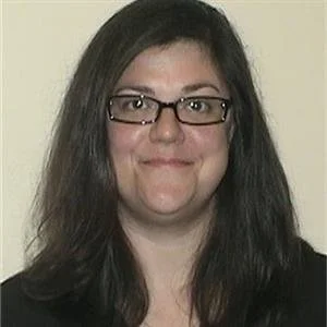 A woman with long dark hair wearing glasses and a black top, smiling at the camera.