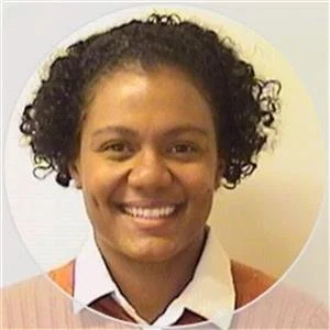 Smiling woman with curly hair wearing a white shirt and an orange top, photo taken indoors.