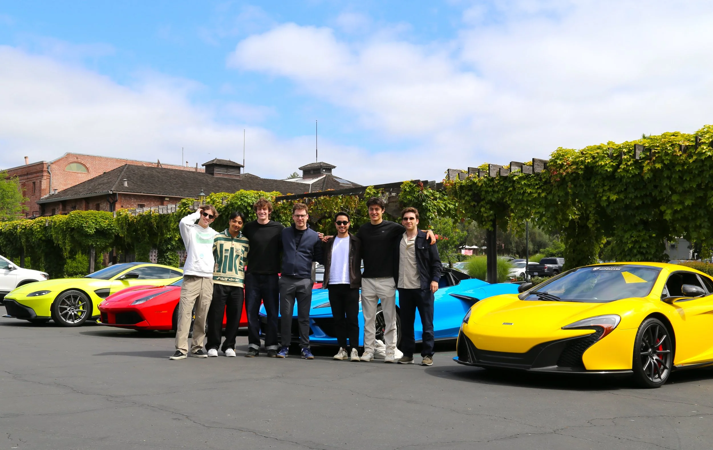A group of men standing next to several high end supercars.