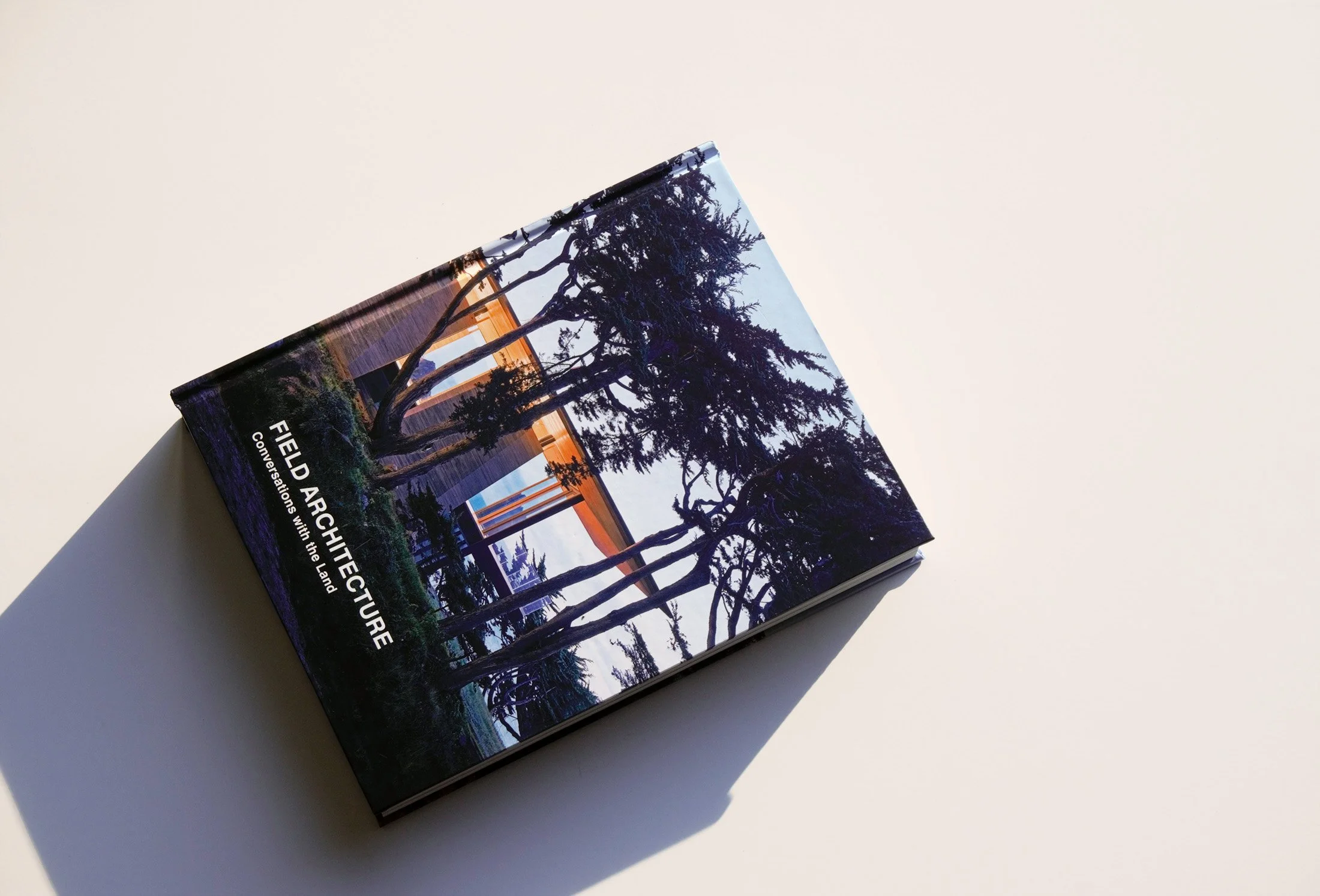Book titled 'Field Architecture: Conversations with the Land' on a light surface, featuring a cover image of trees and a modern building.