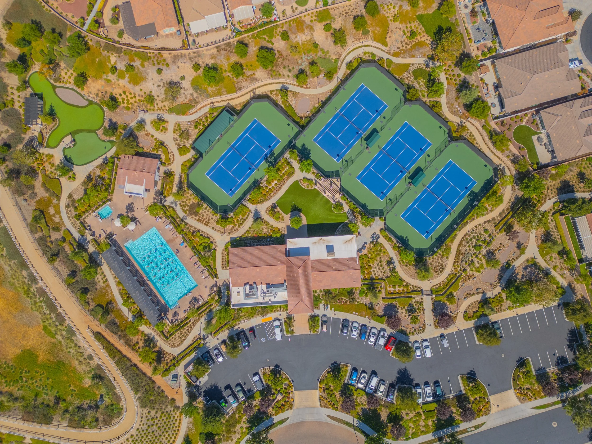 An aerial view of a residential community with tennis courts, a swimming pool, and landscaped areas.