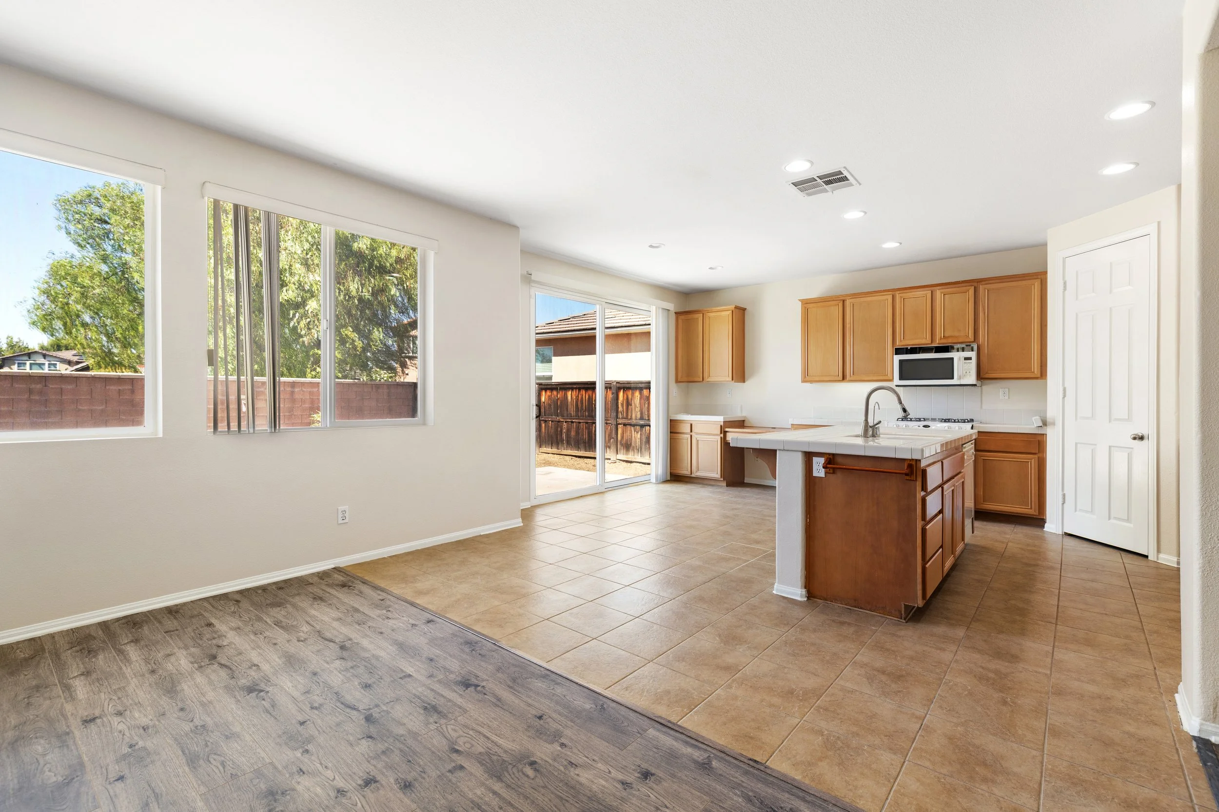 Kitchen and dining area with hardwood and tile flooring, large windows, sliding glass door leading outside, wooden cabinets, microwave, and kitchen island.