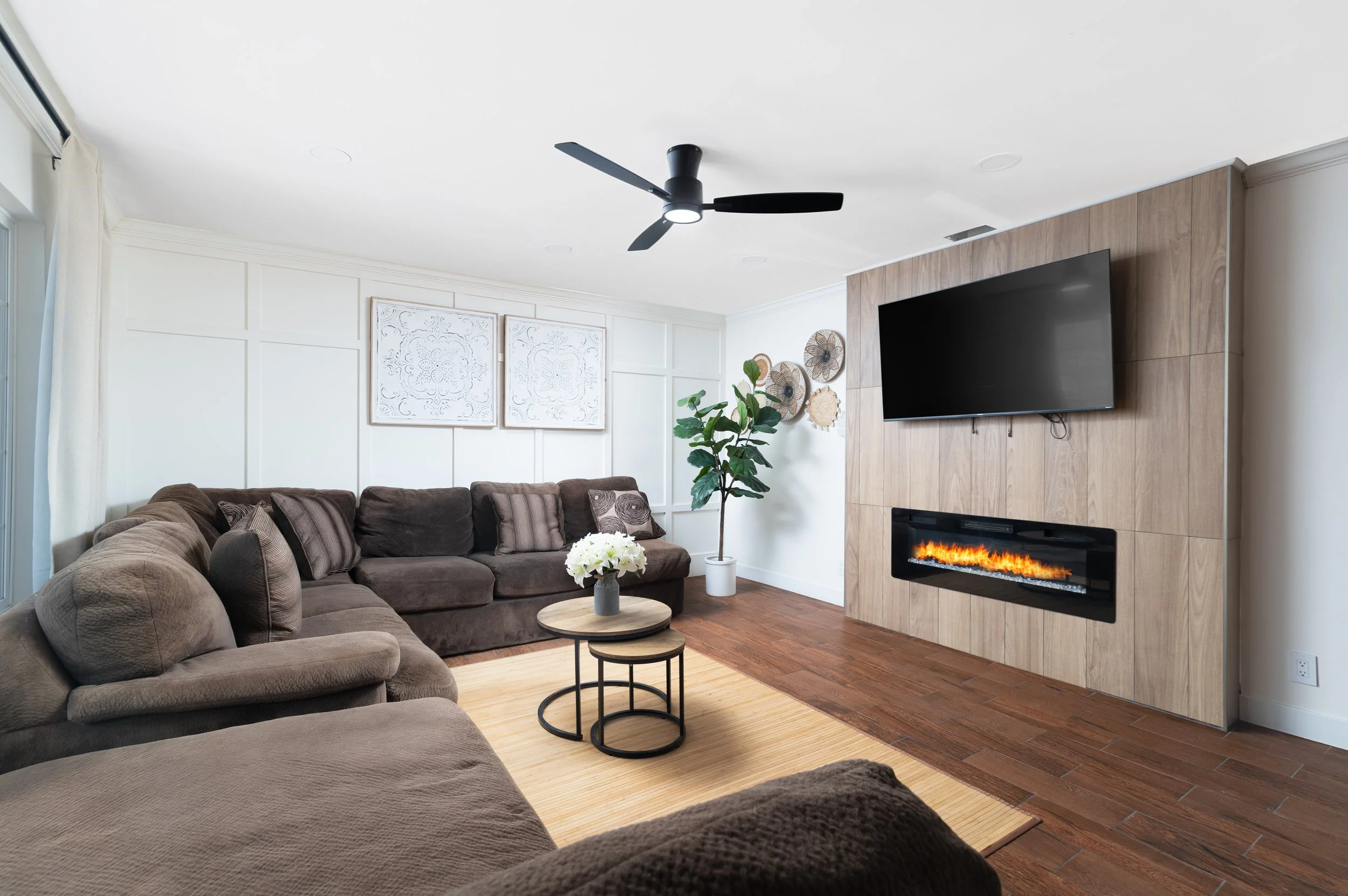 Living room with brown sectional sofa, wall-mounted TV above a built-in linear fireplace, and round wood coffee tables