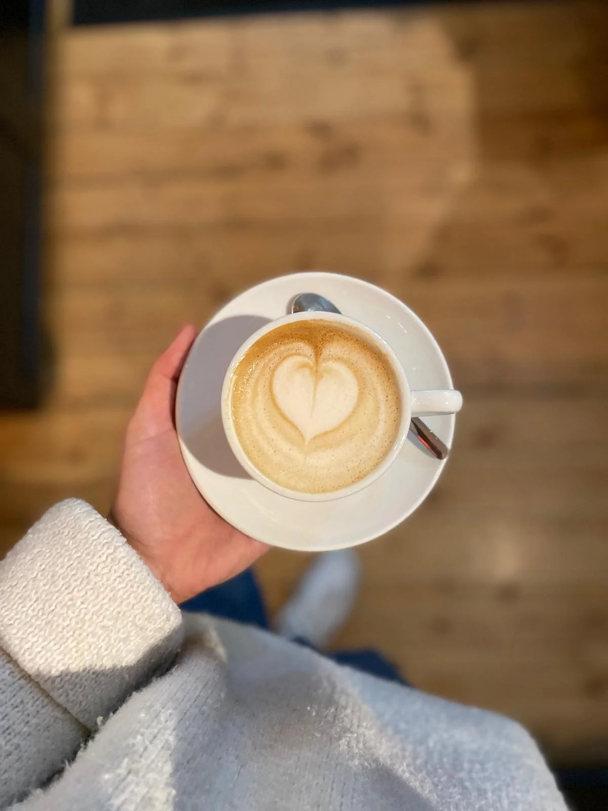 Eine Hand hält eine Tasse Cappuccino mit herzförmiger Latte Art.