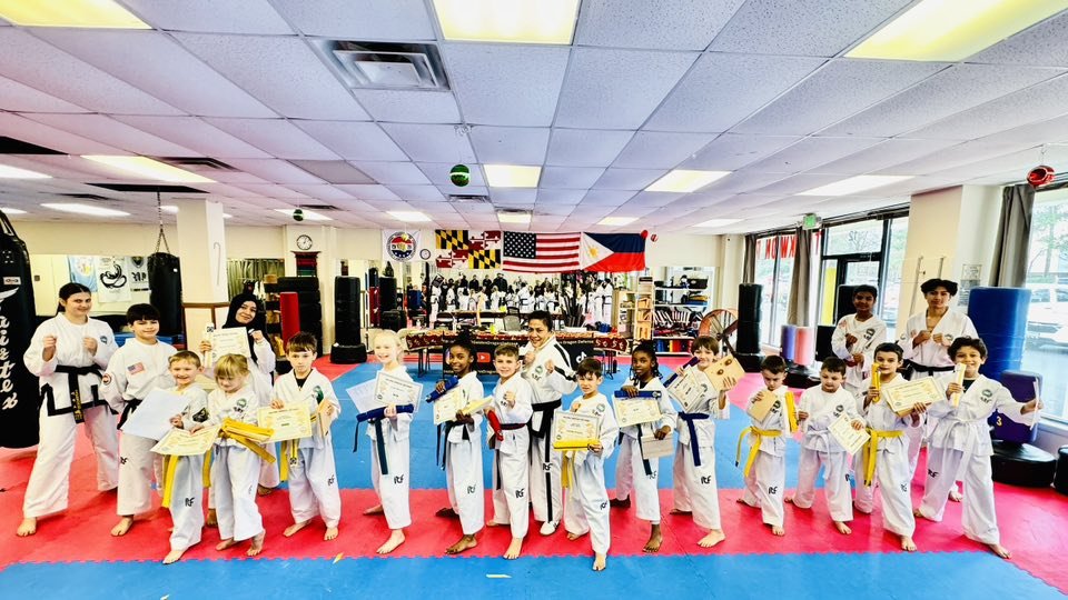 Group of children and instructors in martial arts dojo holding certificates and trophies.