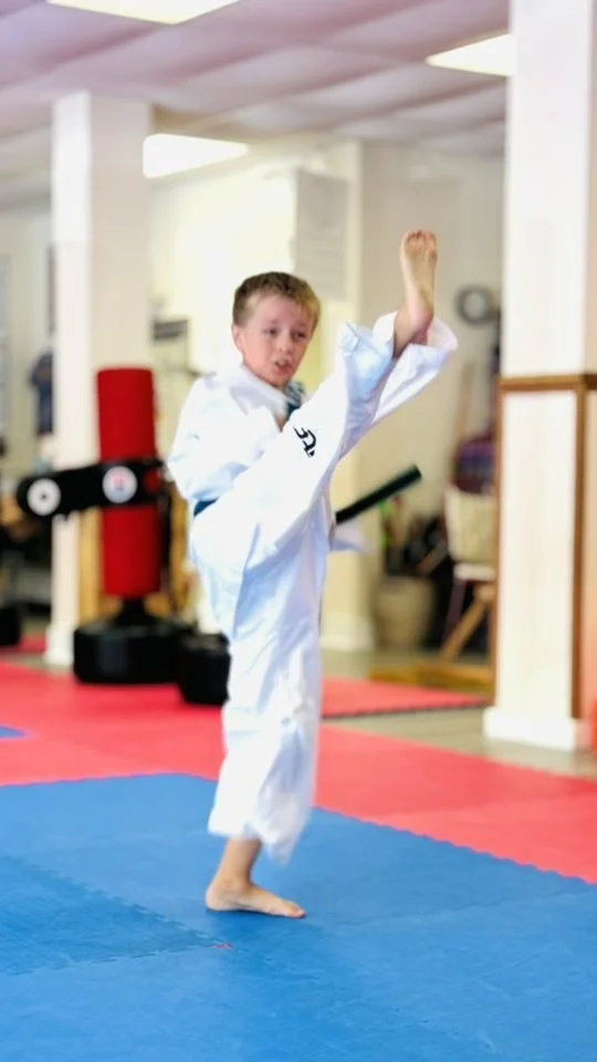 Young boy practicing karate kicks in a dojo, wearing a white gi and focused on his technique.