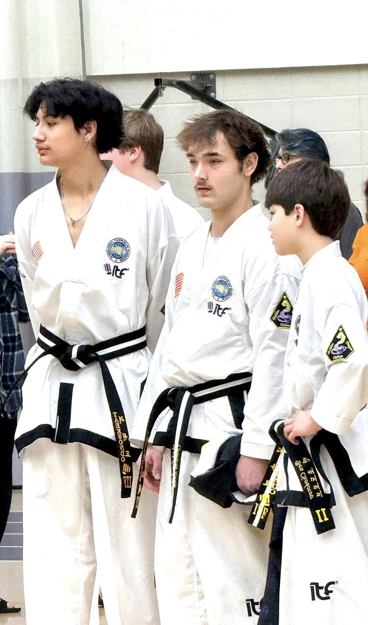 Group of martial artists wearing karate uniforms and black belts, standing together indoors.